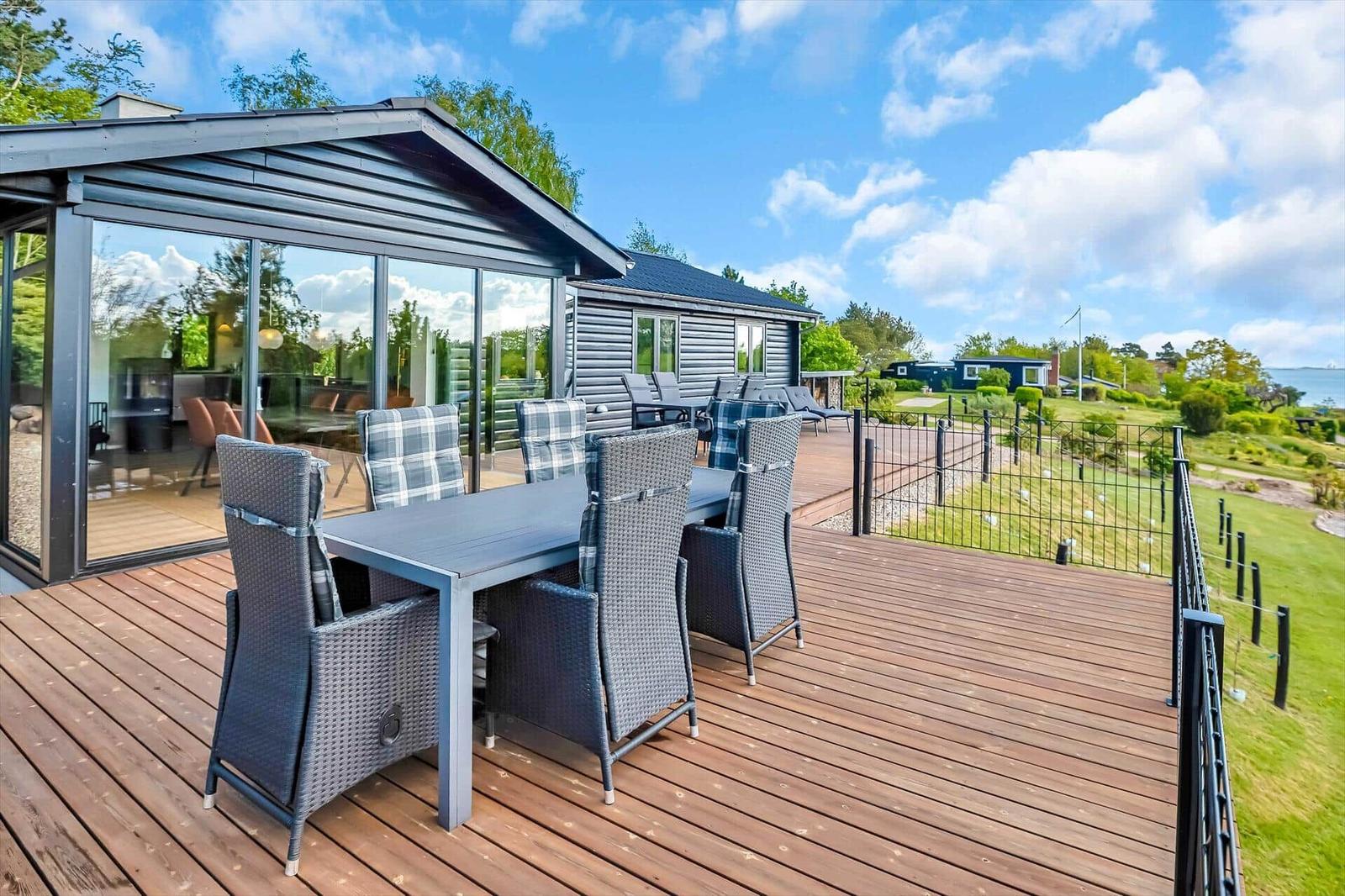 Deck with table and chairs, view of lawn and sea.