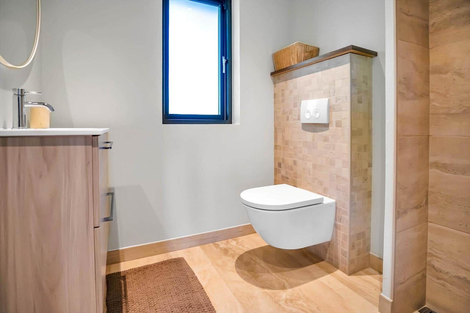 Bathroom with toilet, sink and shower. Wood look and window.