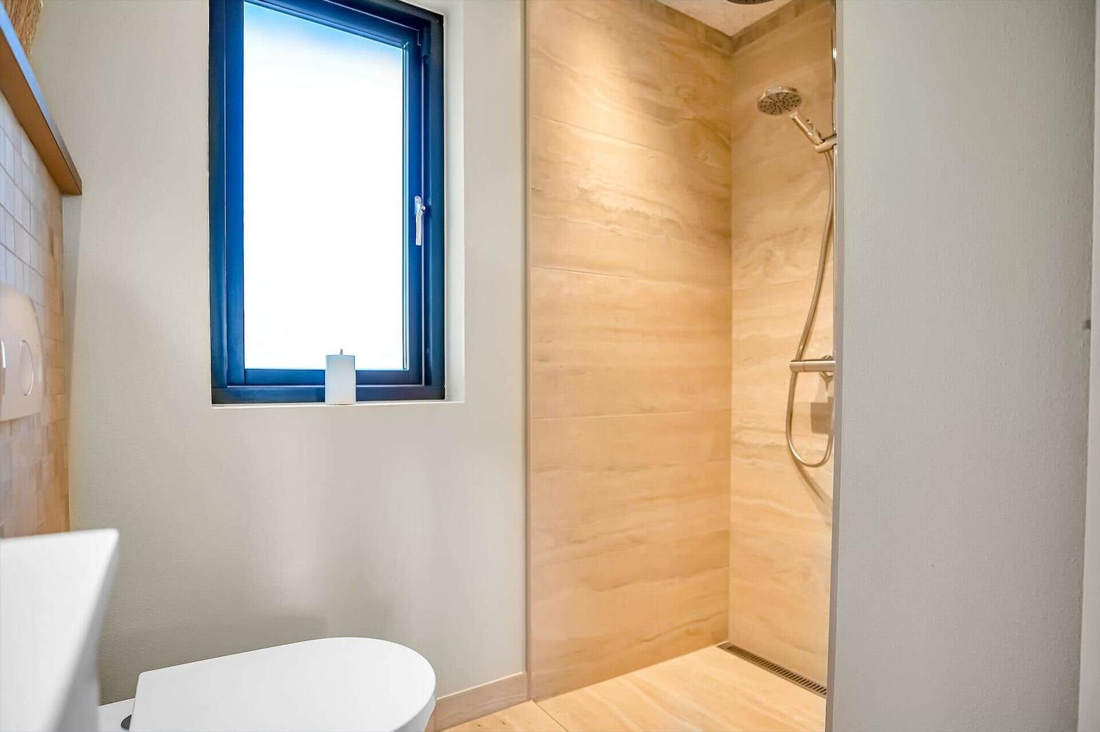 Bathroom with shower, toilet, and window with blue frame.