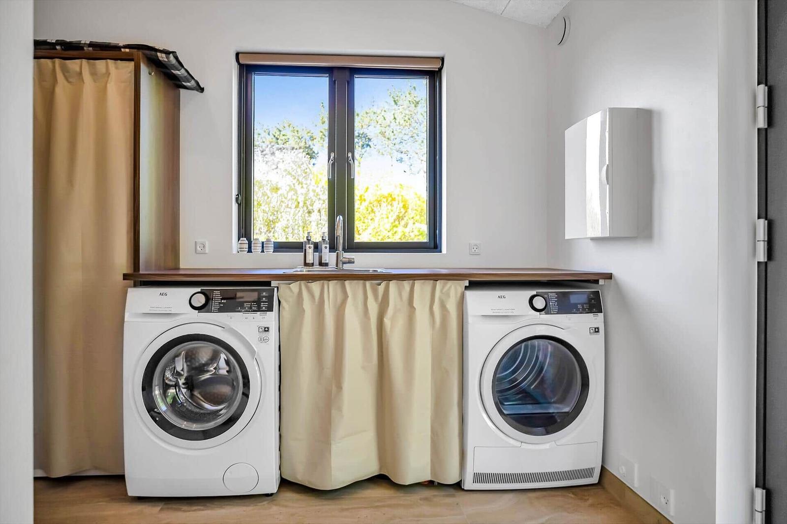 Laundry room with washing machine and dryer under wooden counter with window.