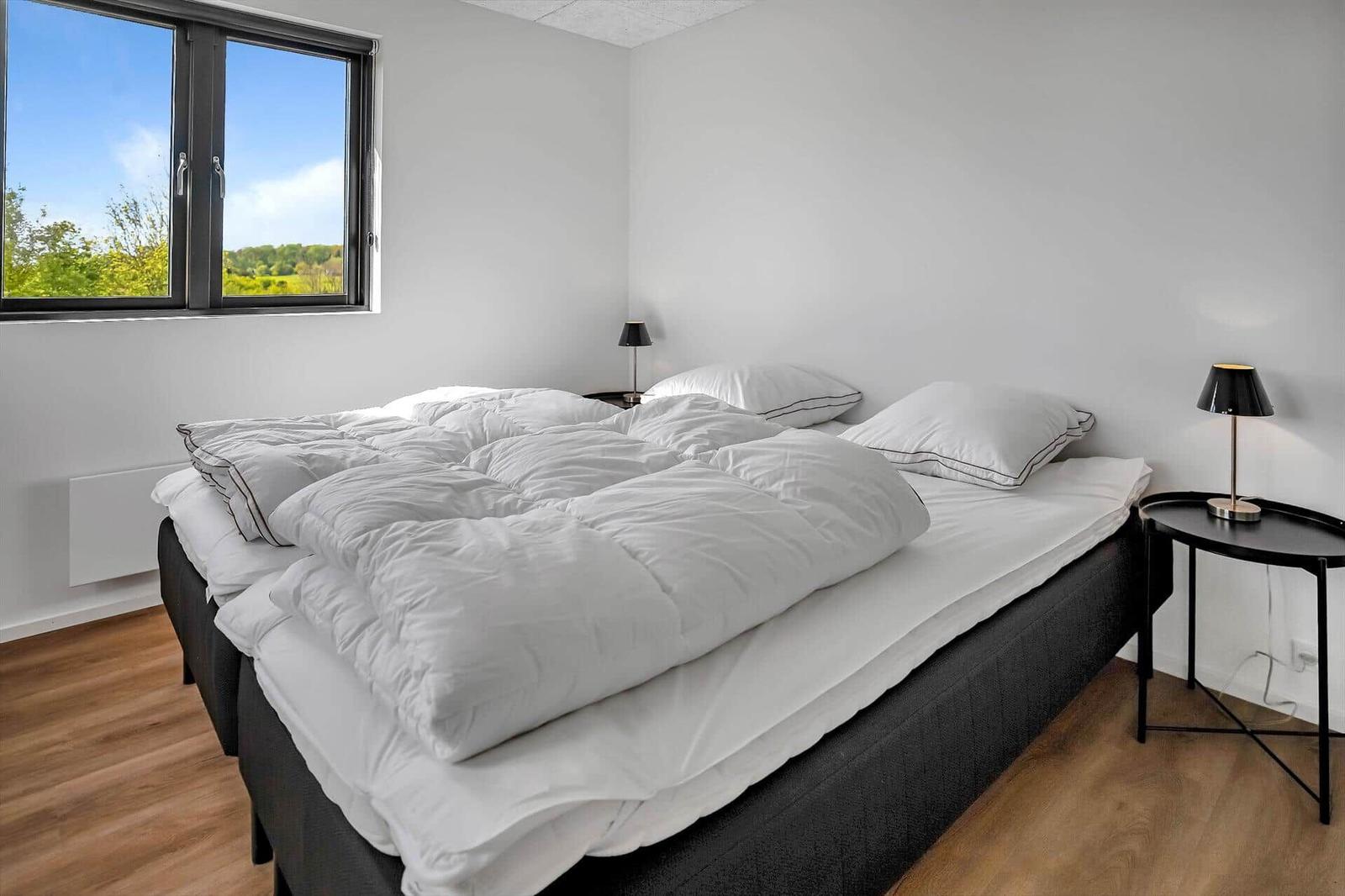 Bedroom with large bed, window overlooking green areas, and two nightstands with lamps.