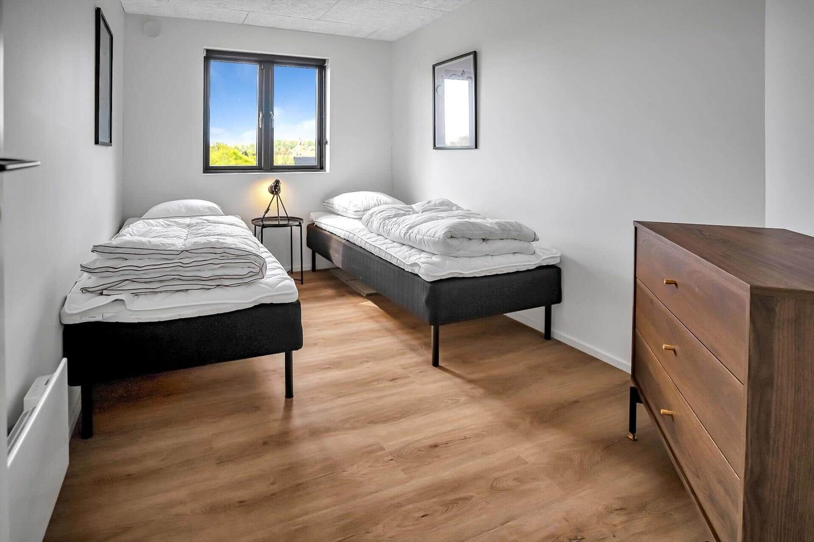 Two single beds, wooden floor, window with view, dresser and wall mirror.