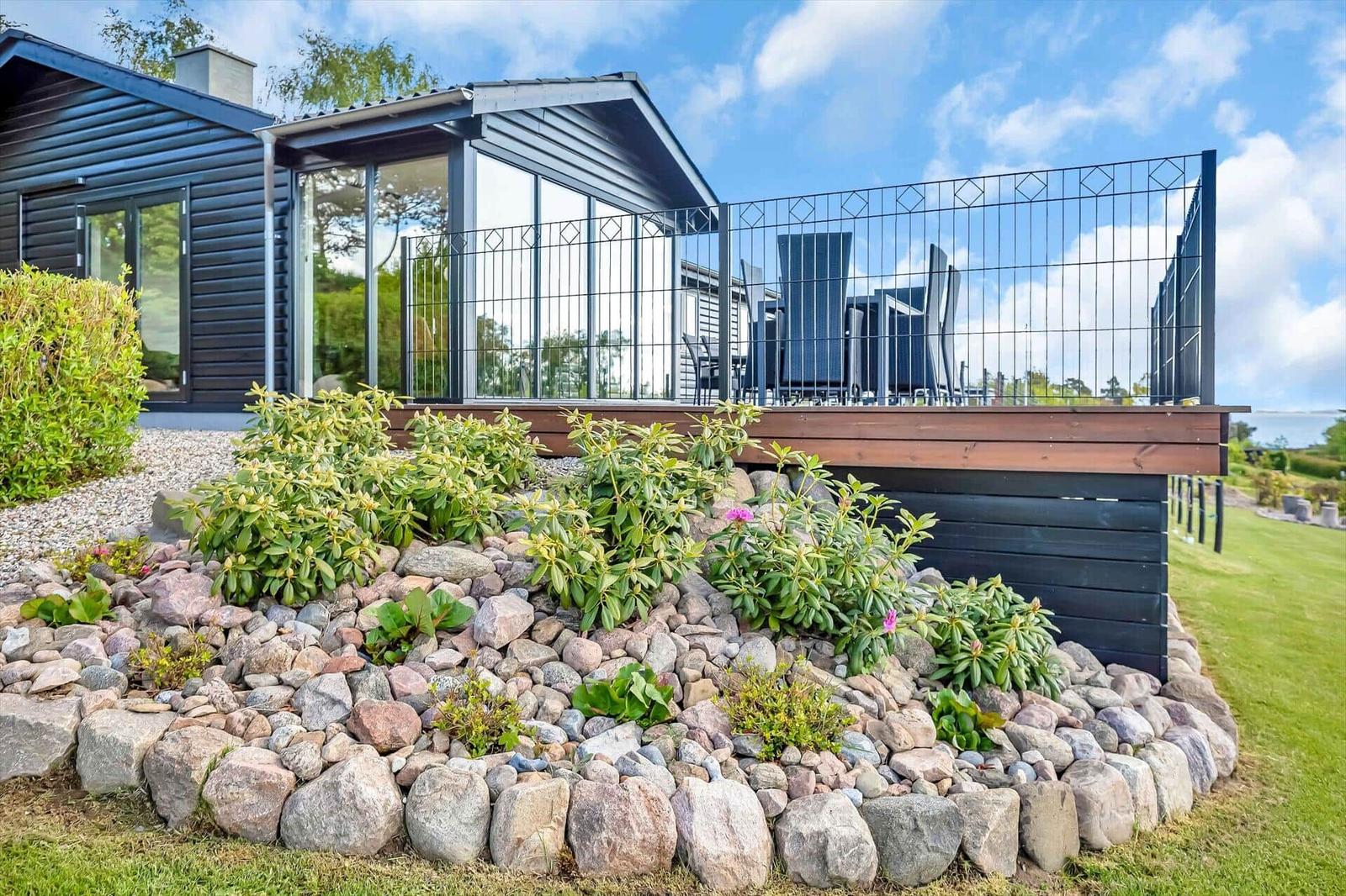 Modern villa with terrace, garden, and stone beds under blue sky.