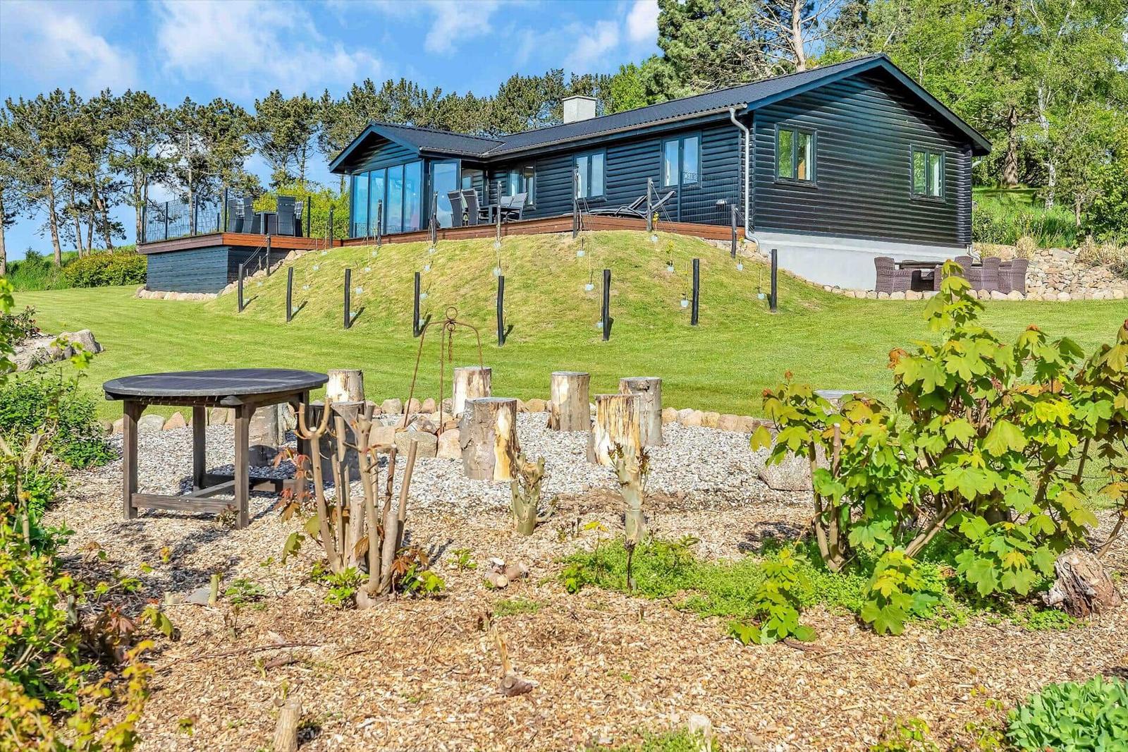 Modern house with terrace and garden. Wooden tables and chairs in the foreground.