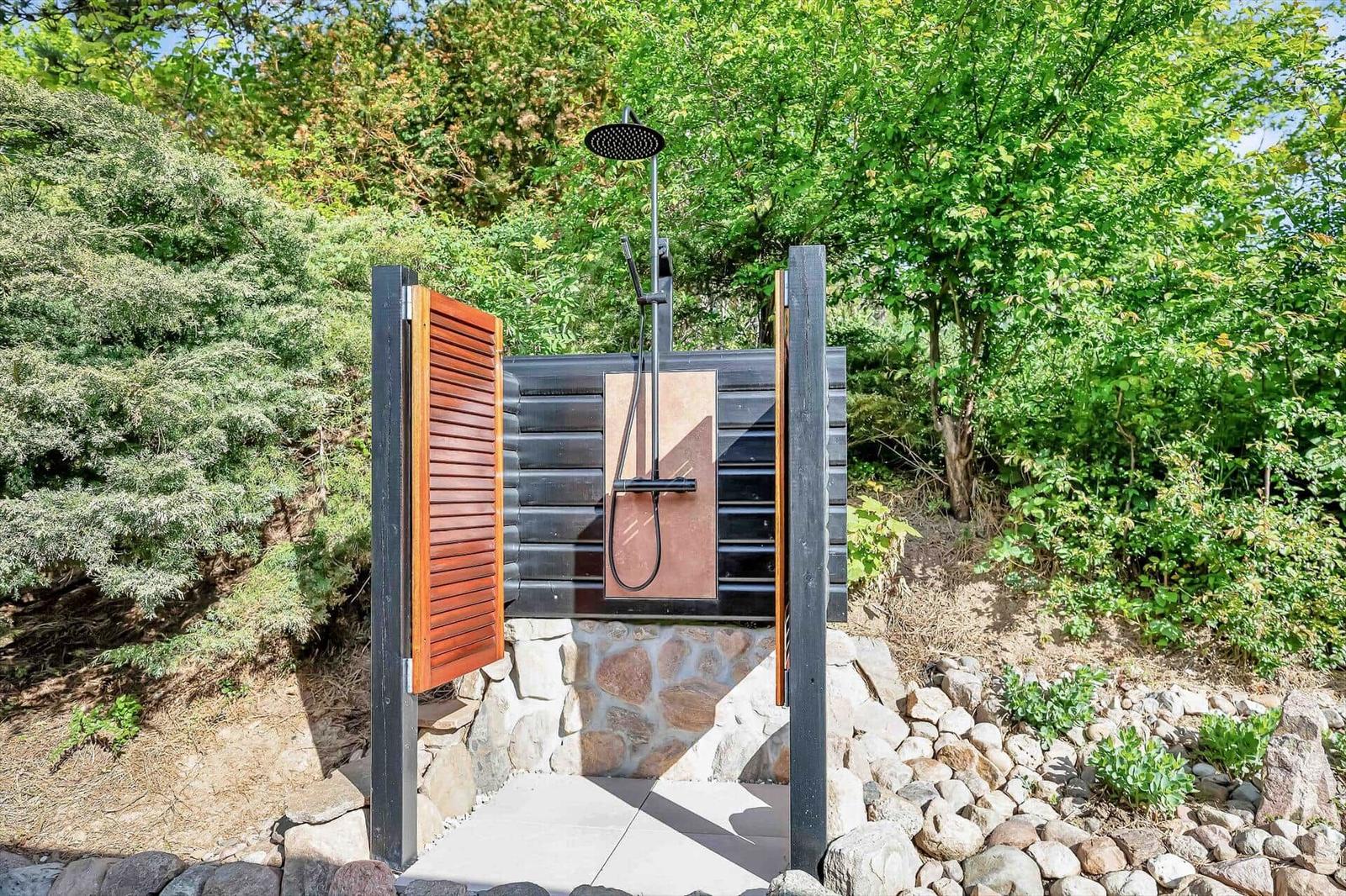 Outdoor shower with wooden door and stone base in green surroundings