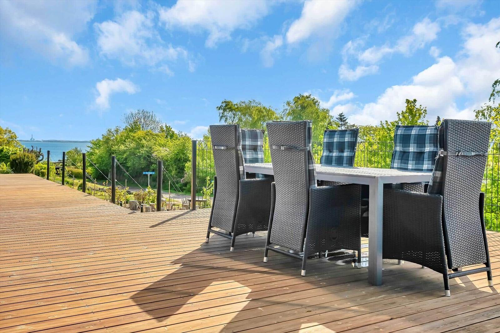 Deck with table and chairs, view of water and greenery.