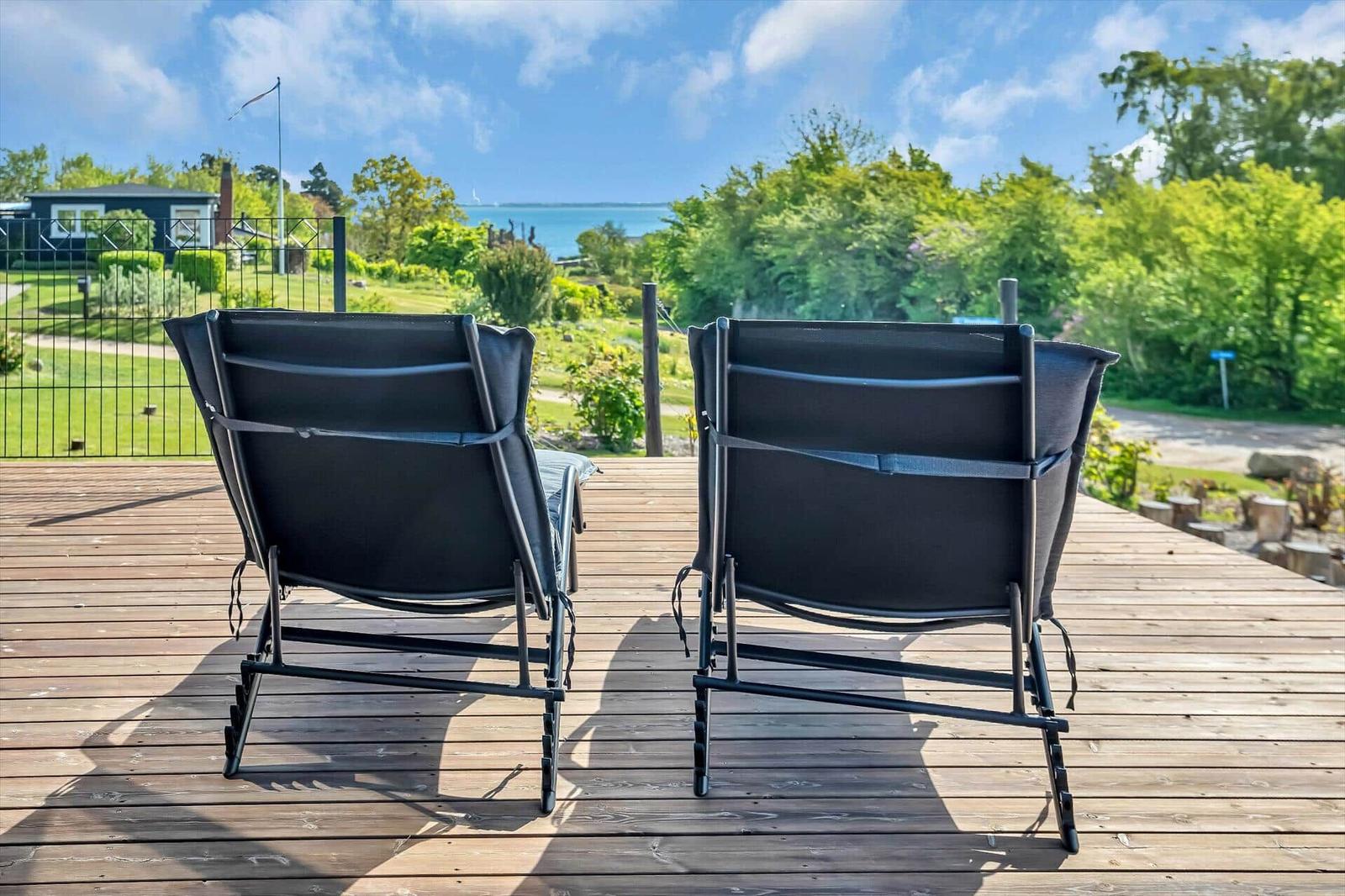 Two black lounge chairs on a wooden terrace with view of green areas and water.