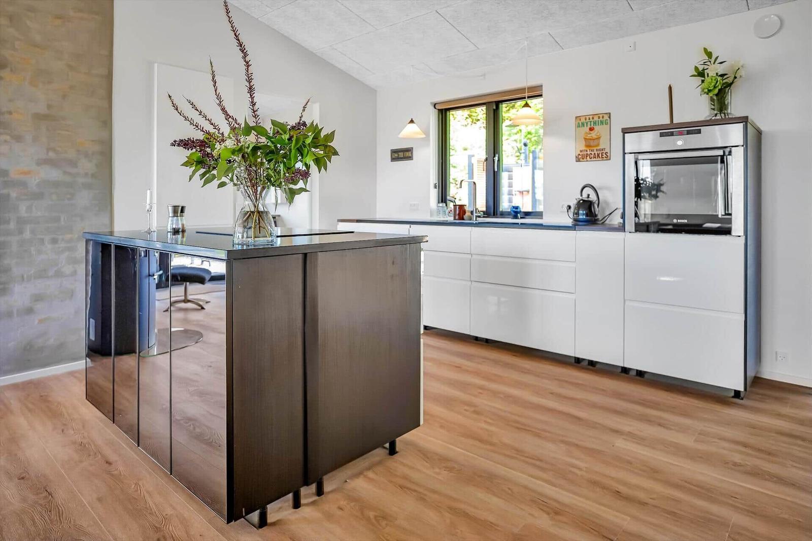 Modern kitchen with island, white cabinets, and wooden floor.
