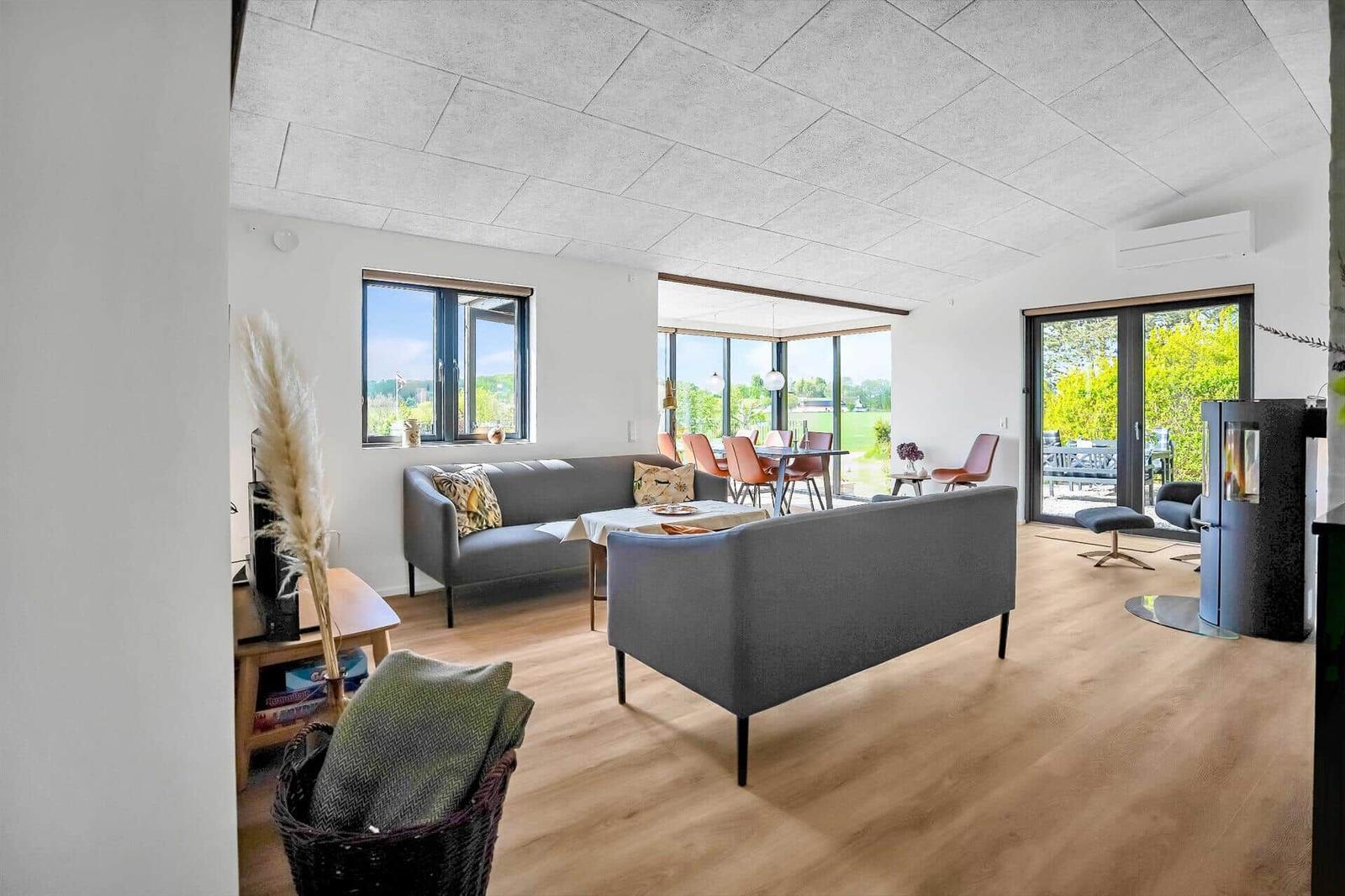 Living and dining area with sofa, table, and windows. Wooden floor and modern furnishings.