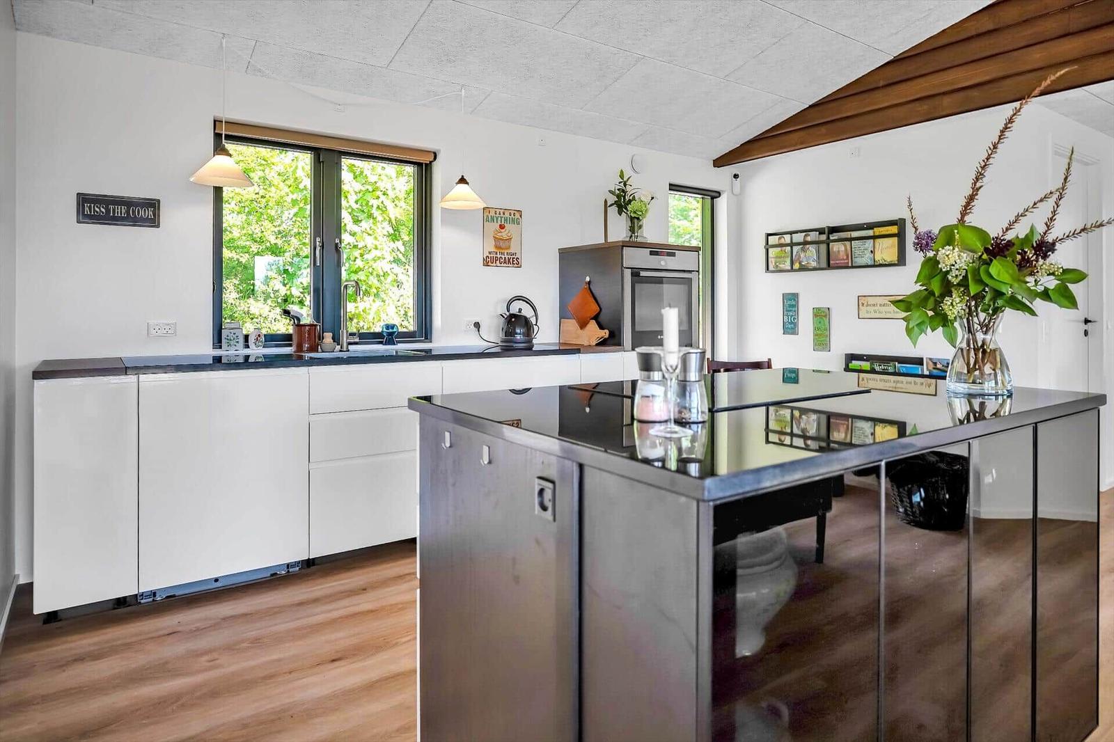 Modern kitchen with island, white cabinets, and wooden floor. Windows with view of greenery.