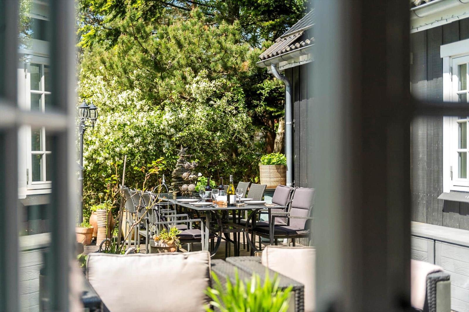 Terrasse mit Tisch, Stühlen und Pflanzen. Blick auf grüne Bäume und Hauswand.