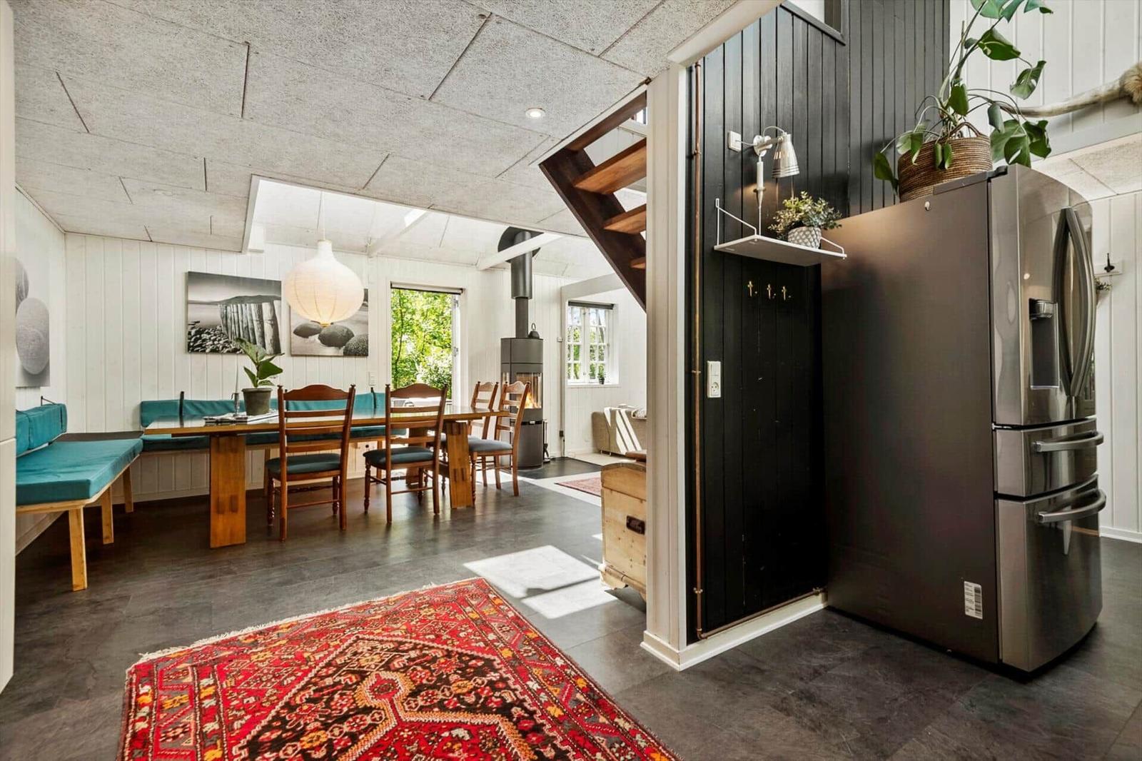 Küche mit Edelstahlkühlschrank, Essbereich mit Holztisch und Sitzbank, roter Teppich, schwarz lackierte Tür.