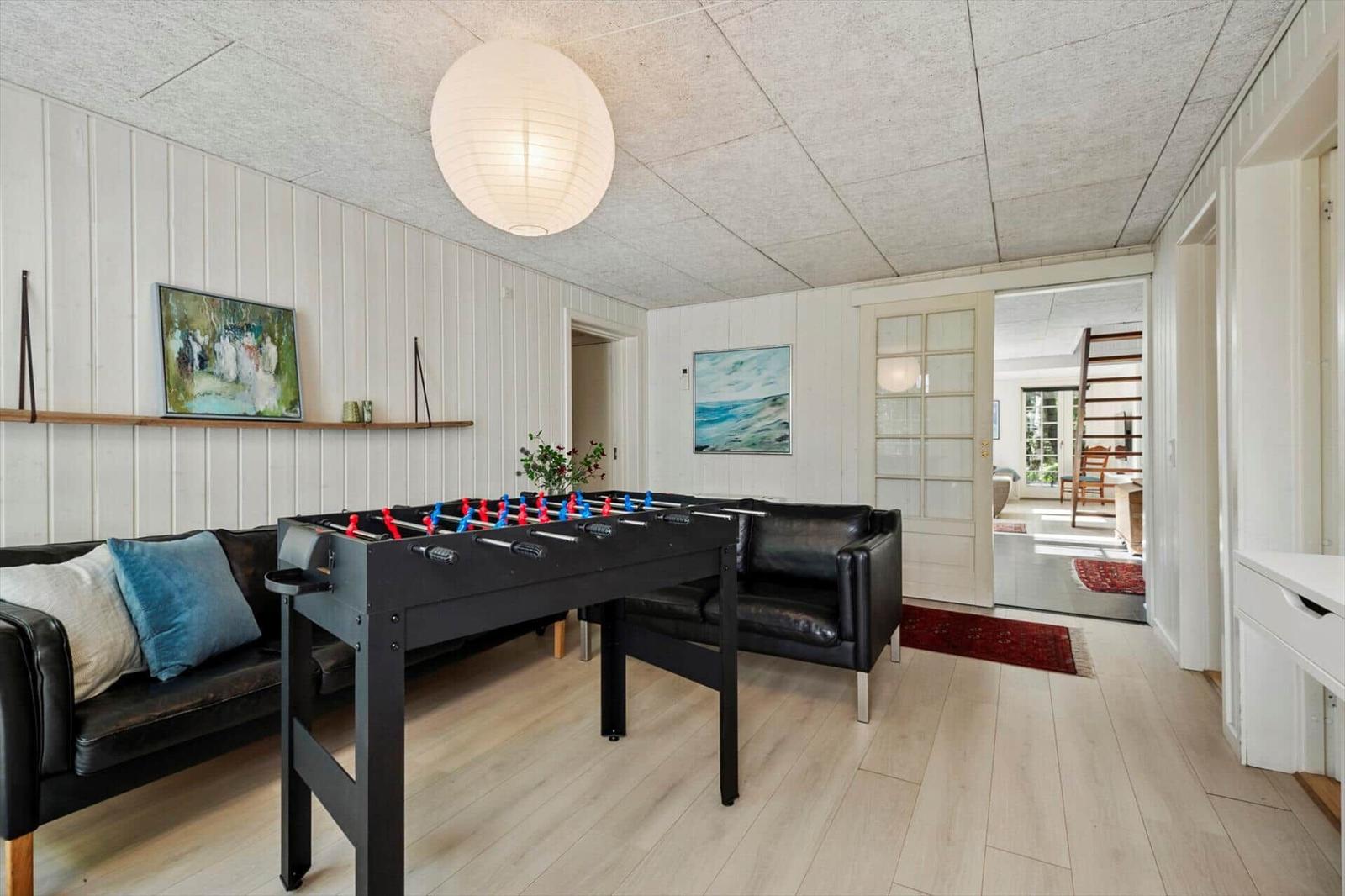 Ein Raum mit einem Tischfußballtisch, schwarzen Ledersofas und einer Deckenleuchte.