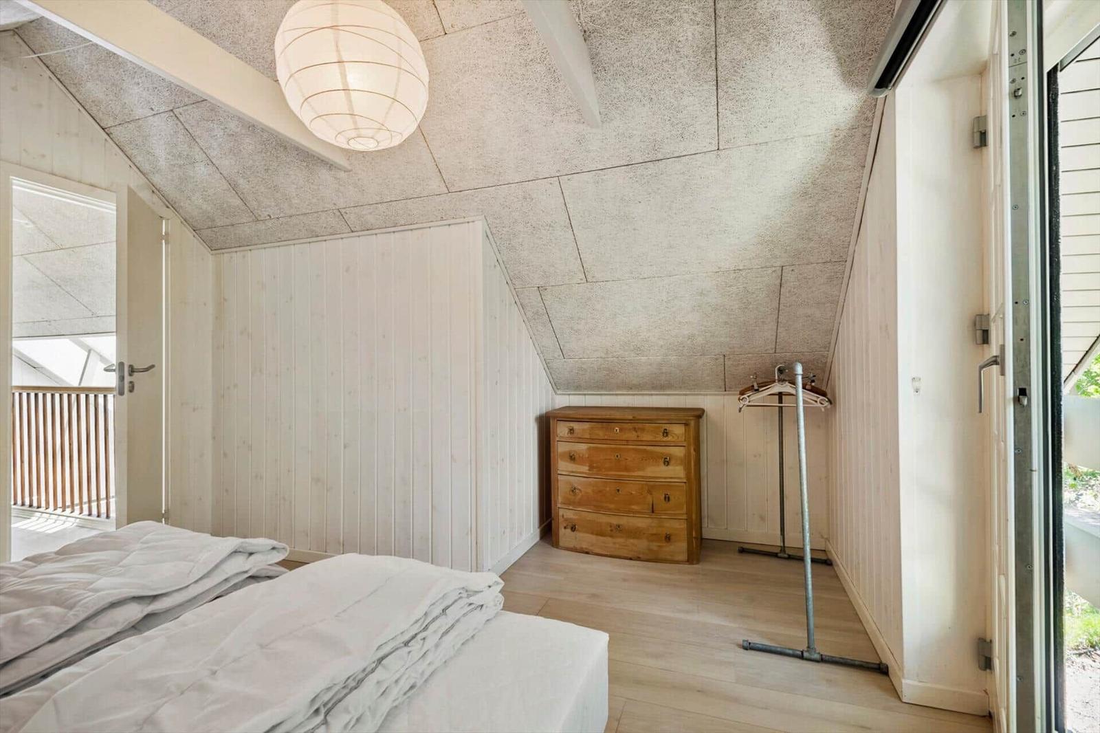 Schlafzimmer mit Bett, Schrank und Kleiderständer unter schrägem Dach