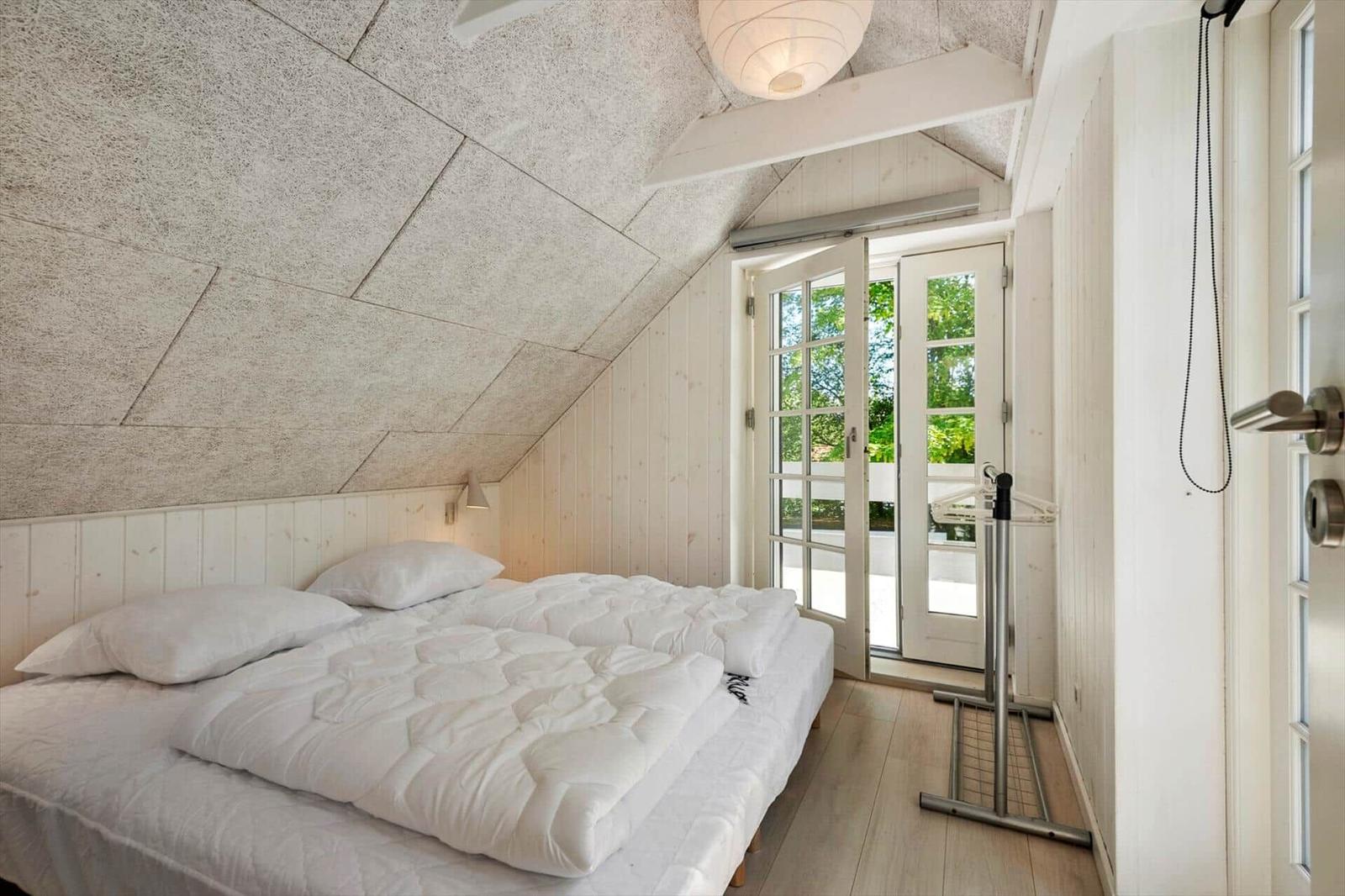 Schlafzimmer mit Doppelbett, weißen Wänden und Fenster zur Terrasse.