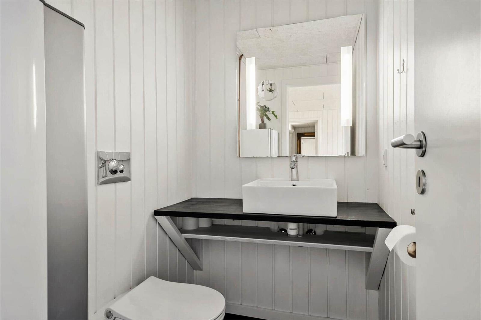 Badezimmer mit Waschbecken, Spiegel und Toilette. Weiße vertikale Wandverkleidung und schwarzem Unterschrank.