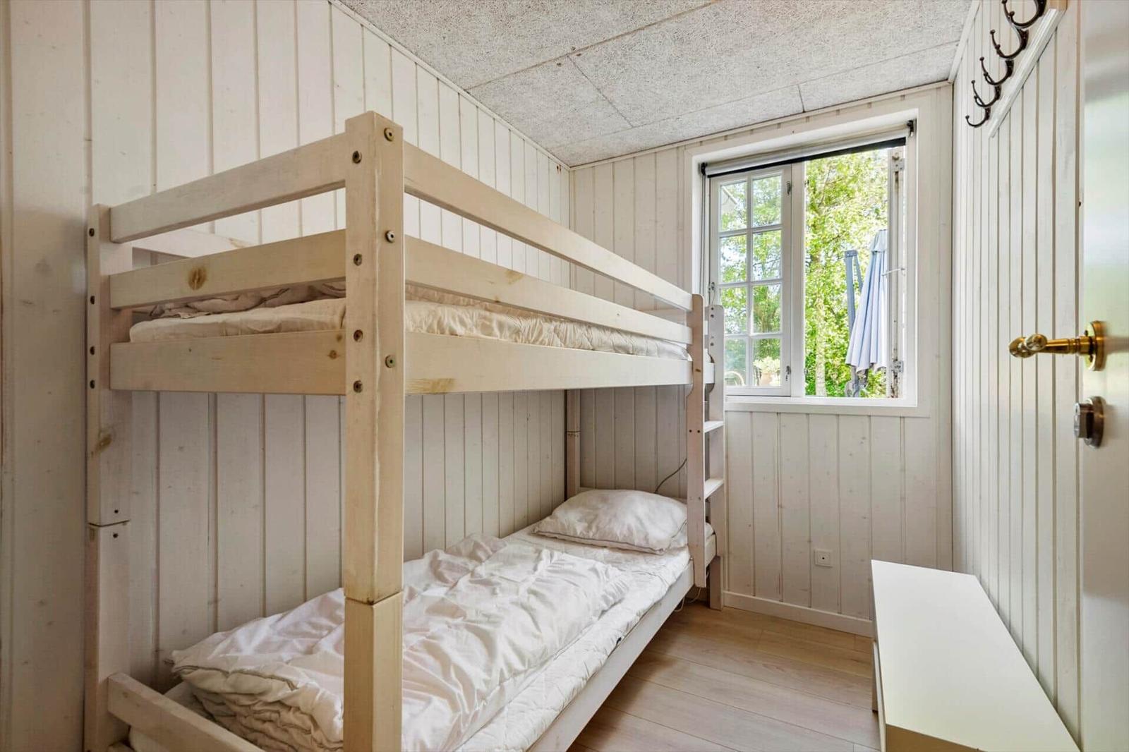 Zimmer mit Doppelstockbett, Fenster und Kleiderhaken an der Wand.