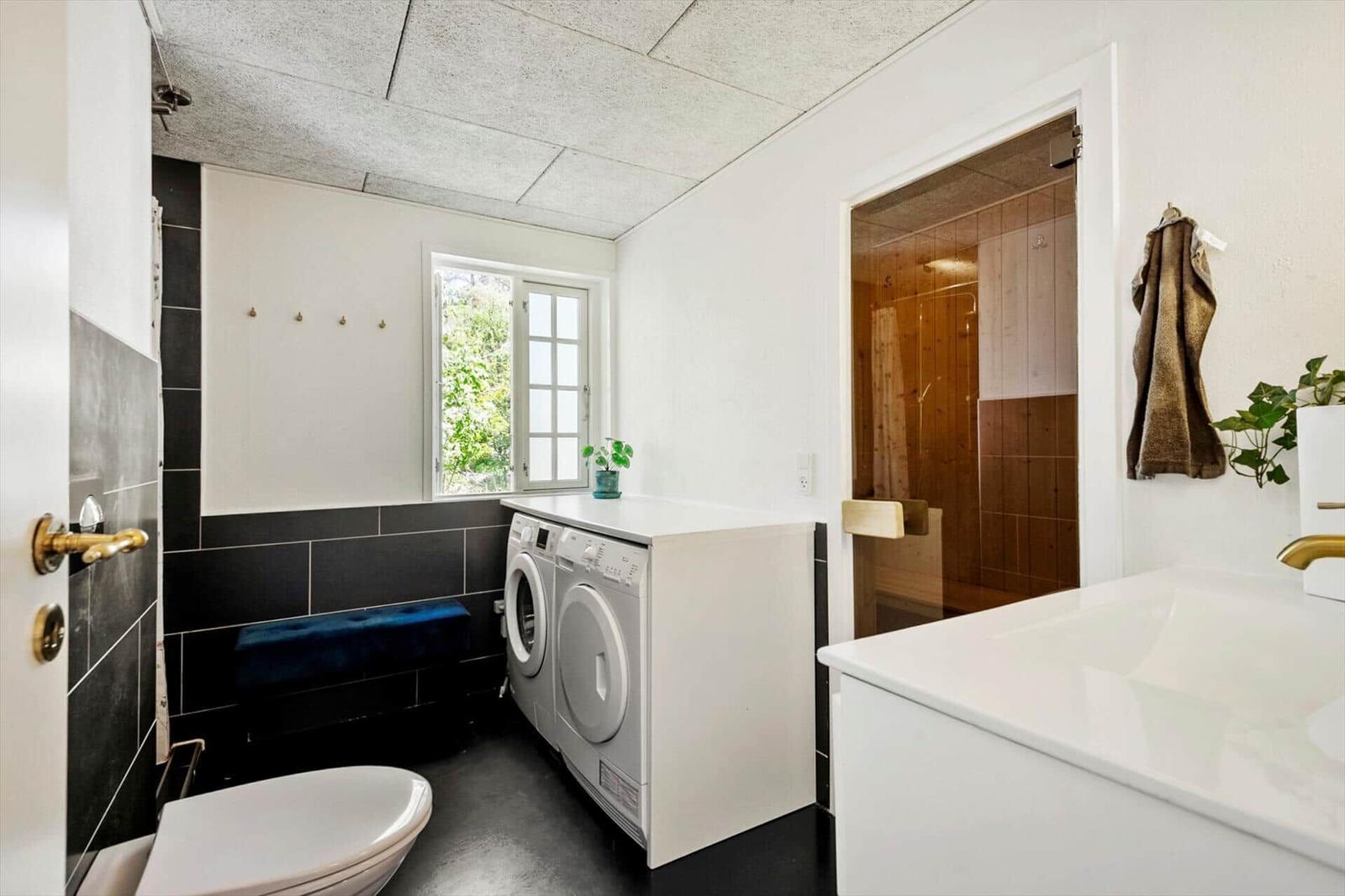 Badezimmer mit Waschmaschine, Dusche und Toilette. Fenster mit Blick auf Grün.