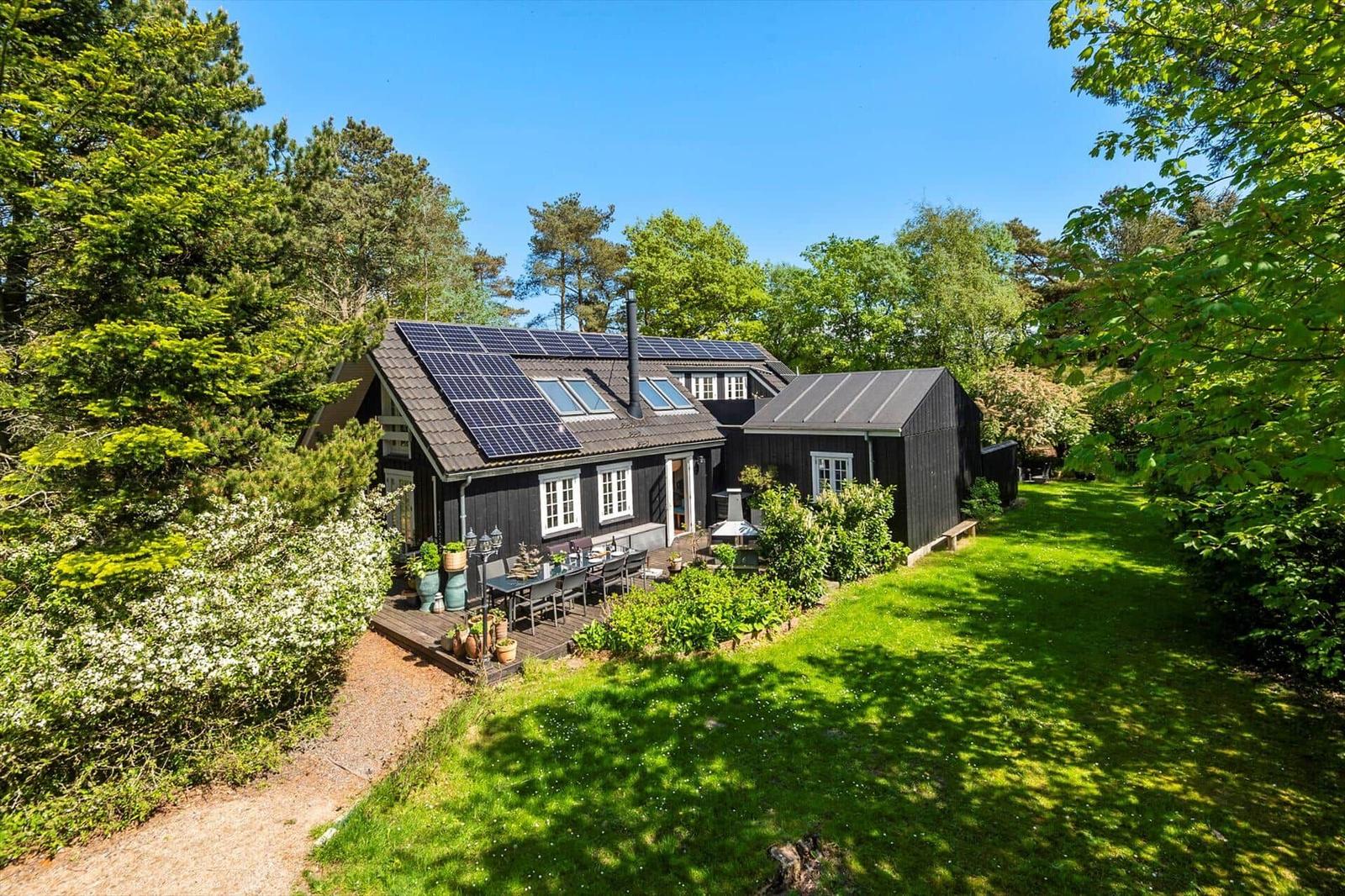 Schwarze Holzhütte mit Solaranlage, Terrasse und Garten in grüner Umgebung.