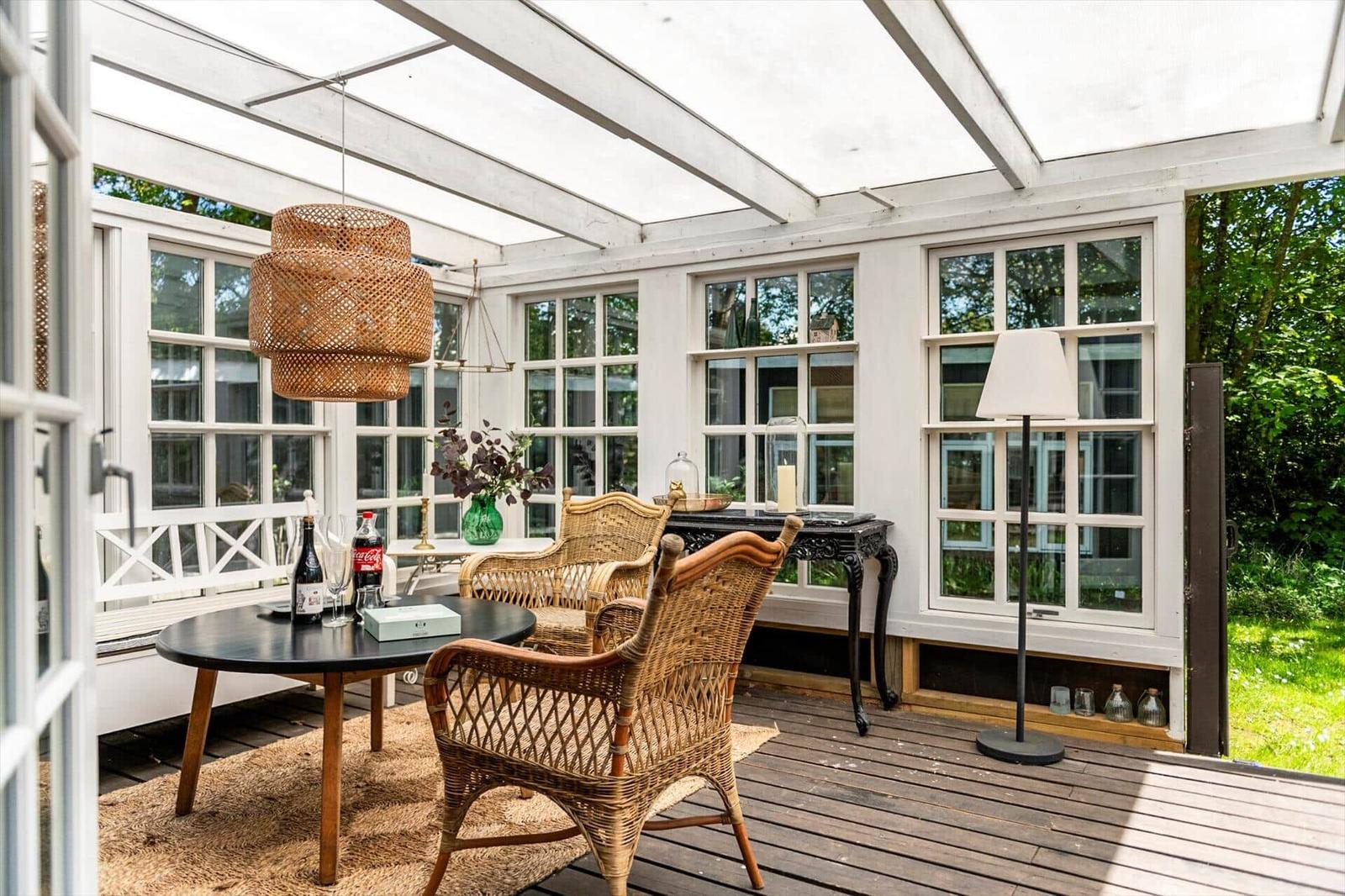 Glasdach über Terrasse mit Stühlen und Tisch. Holzdecke und Fenster sichtbar.