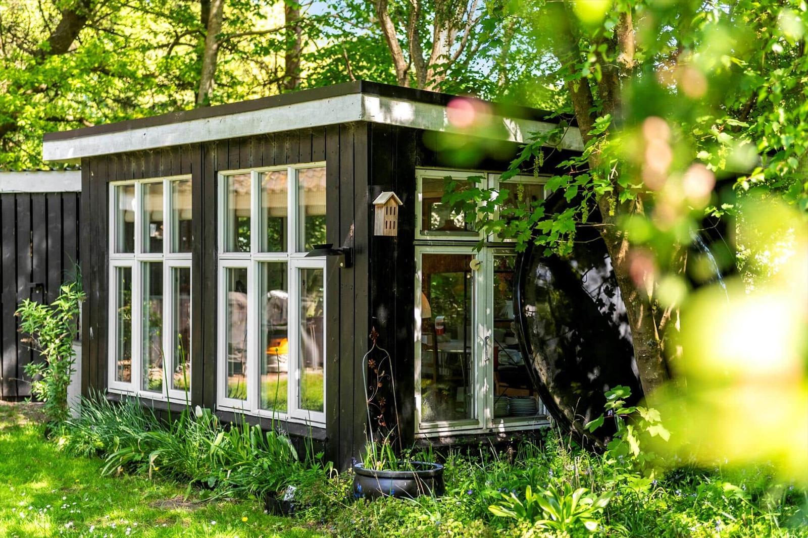 Ein kleines Haus mit großen Fenstern steht im Grünen. Eine Tür führt ins Innere.