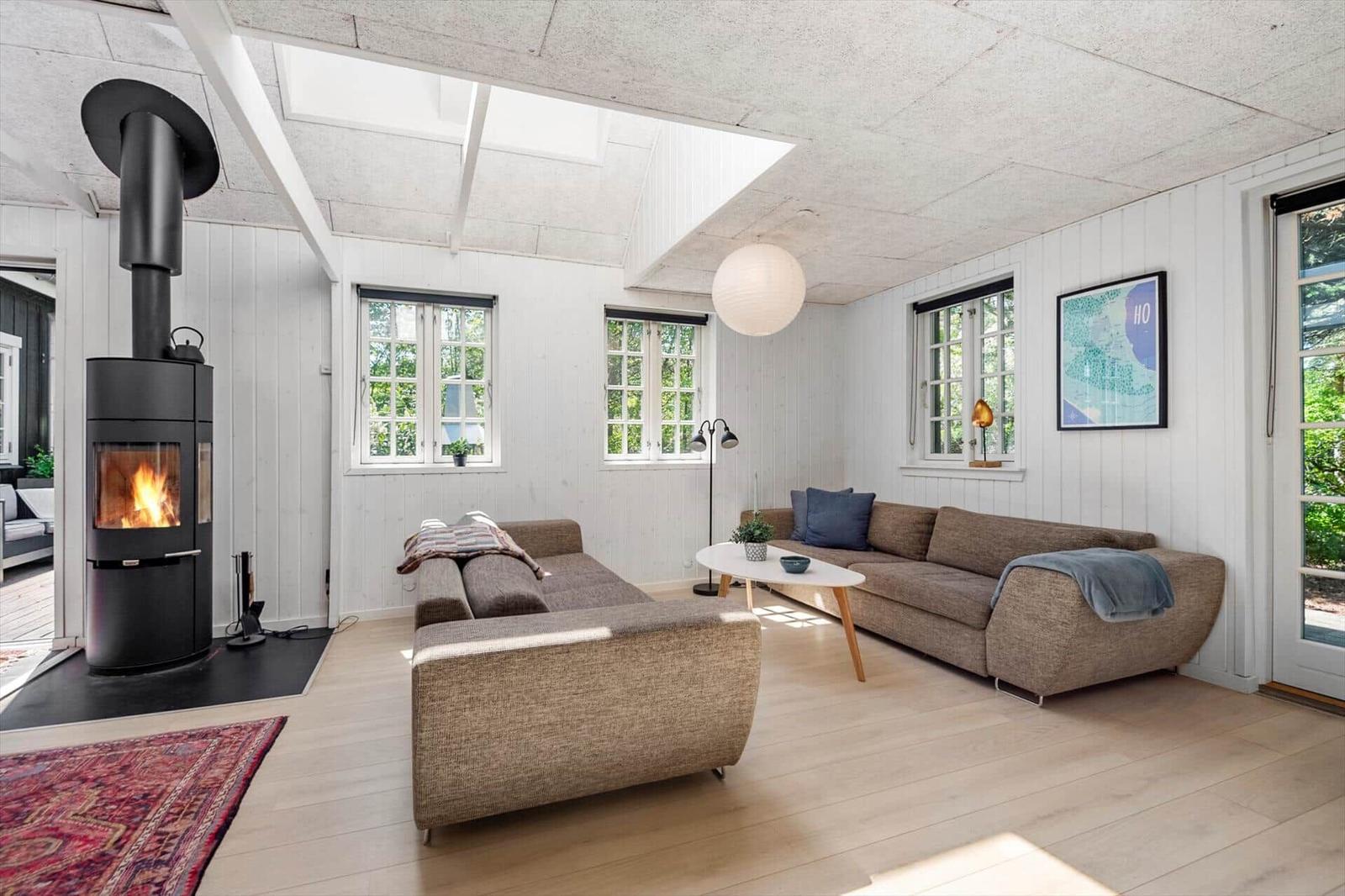 Wohnzimmer mit Kamin, Sofa und Fenstern. Holzboden und weiße Wände.