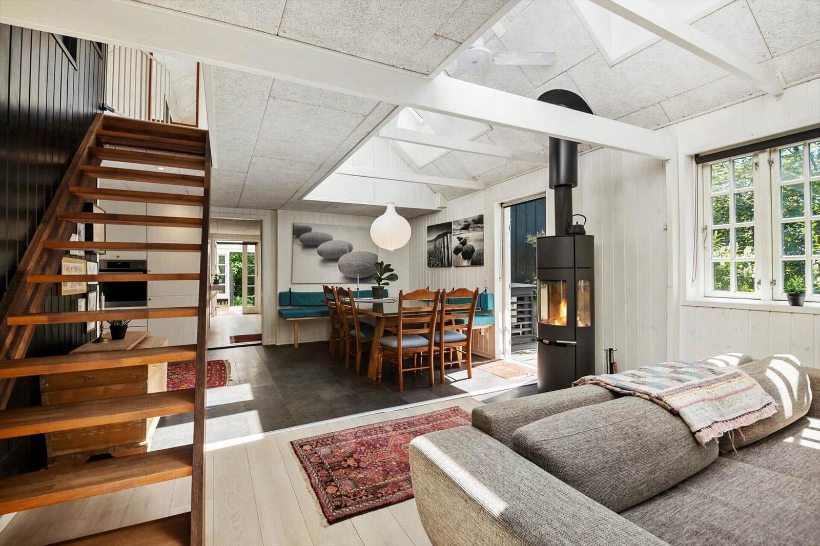 Wohnbereich mit Kamin, Essbereich und Holztreppe. Fenster und Dachfenster.