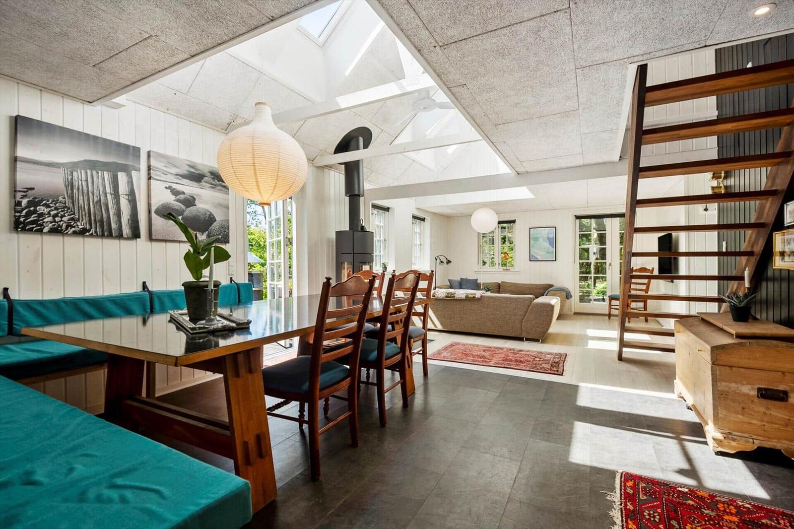 Großes Wohn- und Esszimmer mit Holztisch, Sitzbank und Kamin. Holzstufen und Fenster.