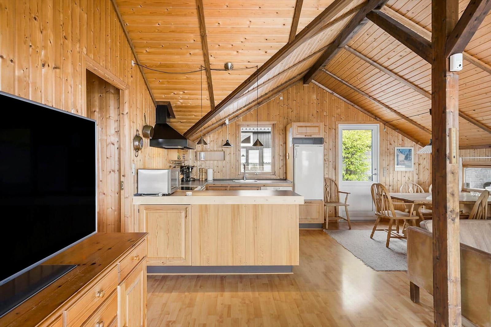 Küche mit Essbereich und Holzdecke. Fernseher, Kühlschrank und Tisch mit Stühlen.