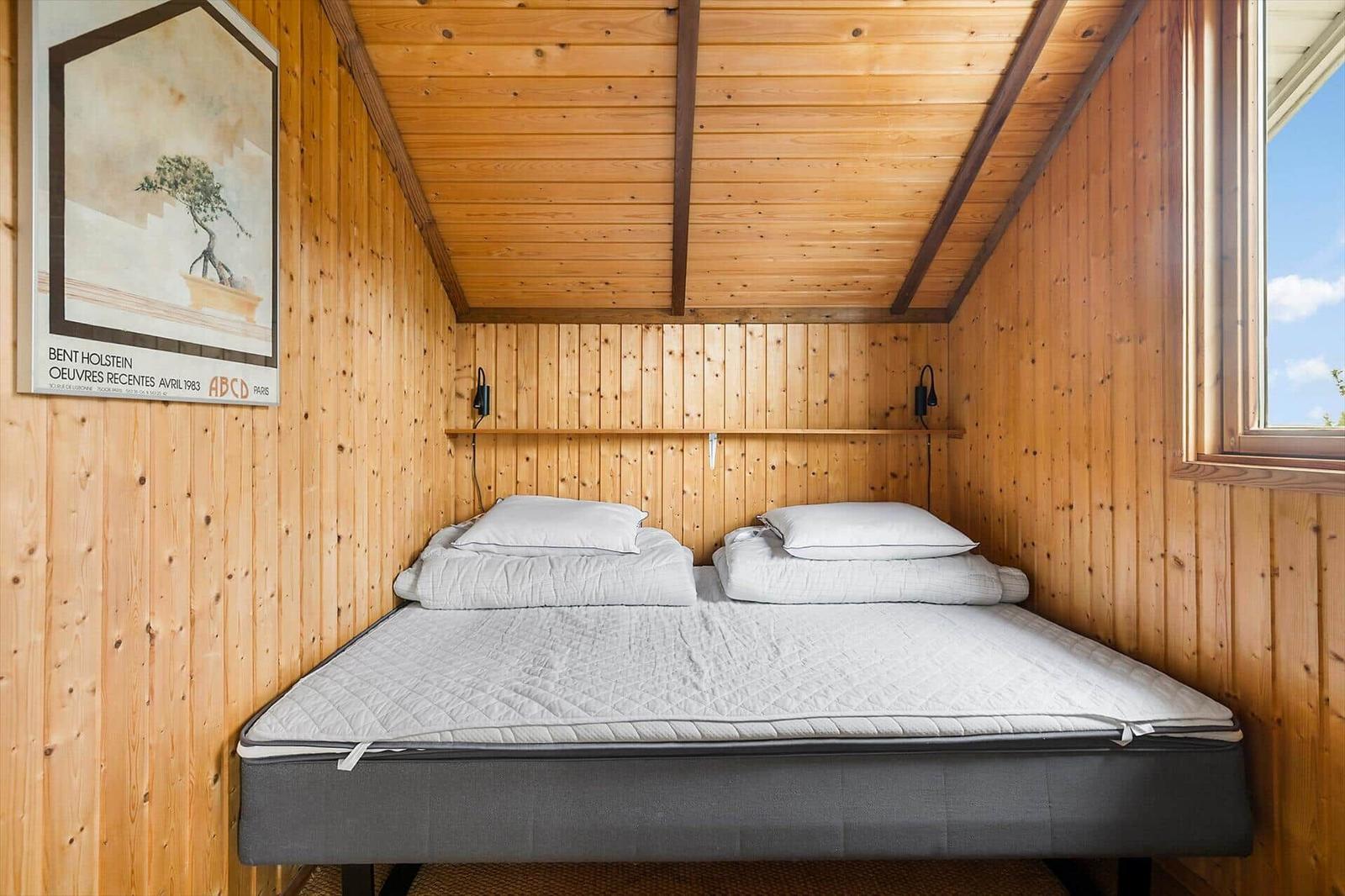Ein Bett mit Matratze und Kissen in einem holzverkleideten Raum mit Fenster und Wandposter.