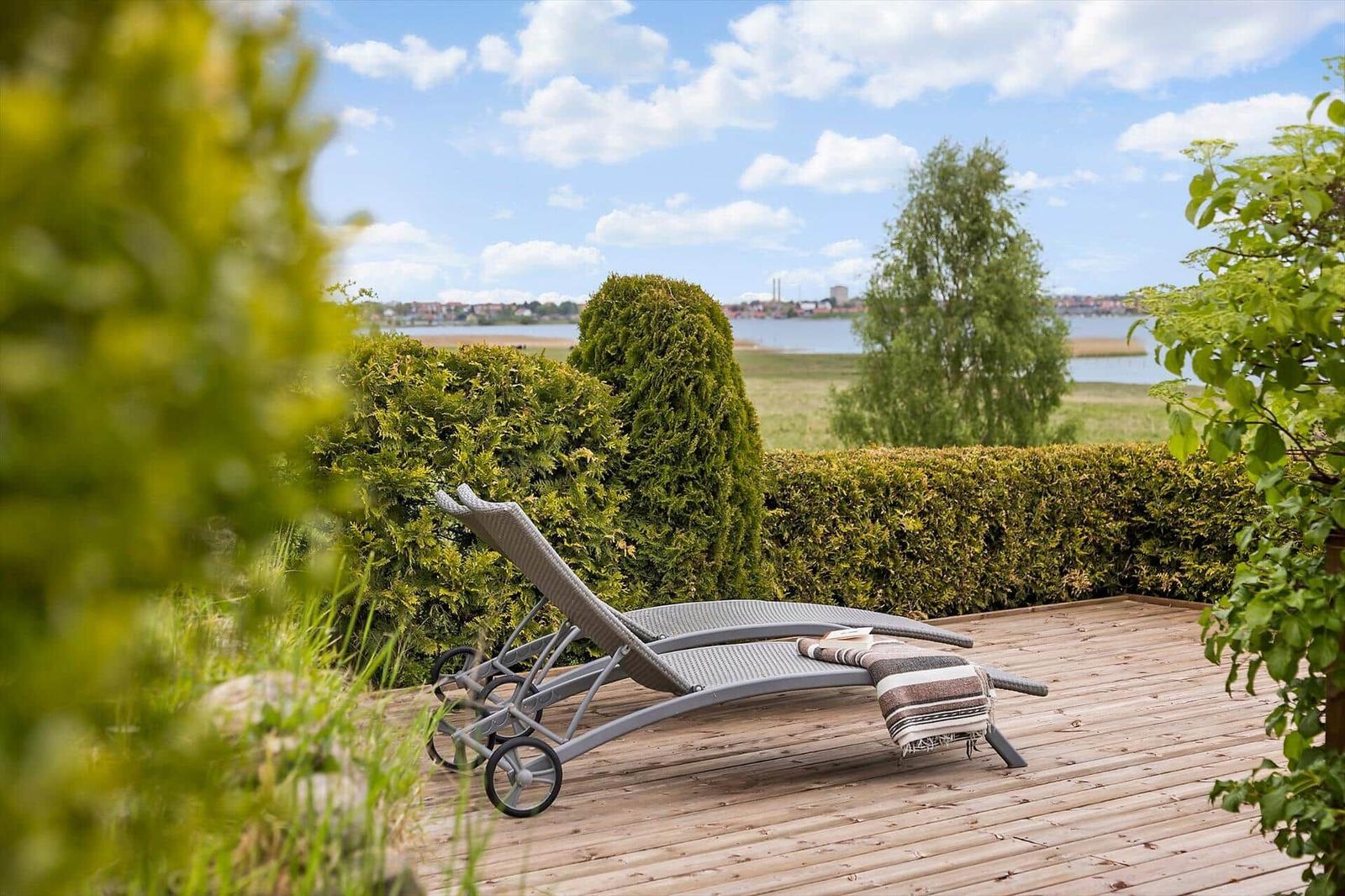 Liegendecke auf Holzterrasse mit Blick auf Wasser und Grün.