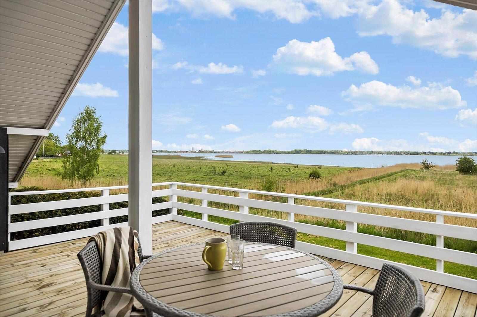 Terrasse mit Tisch und Stühlen. Blick auf Fluss und Grasland unter blauem Himmel.