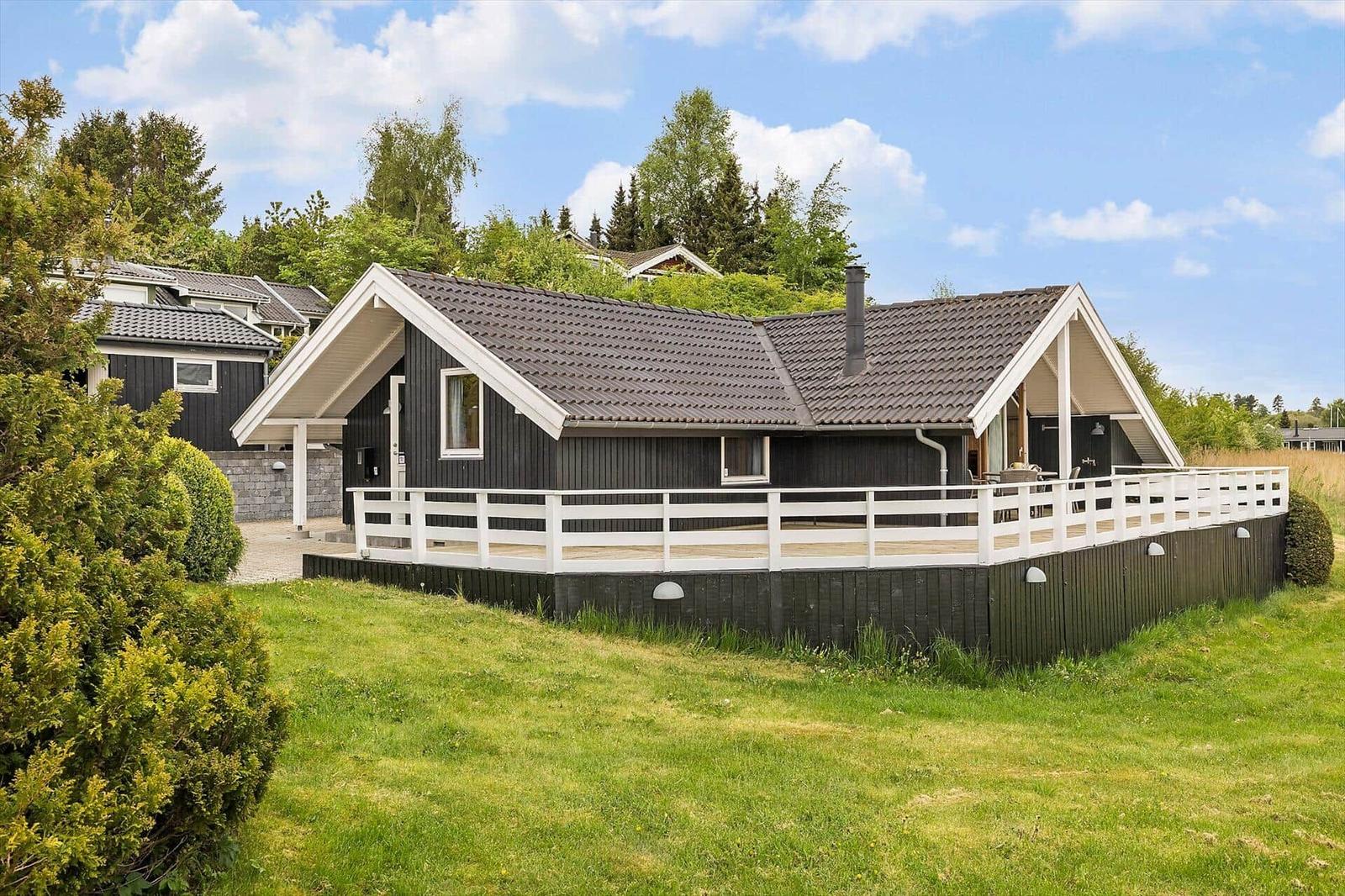 Ein Haus mit dunklem Holz und weißer Veranda im Grünen.