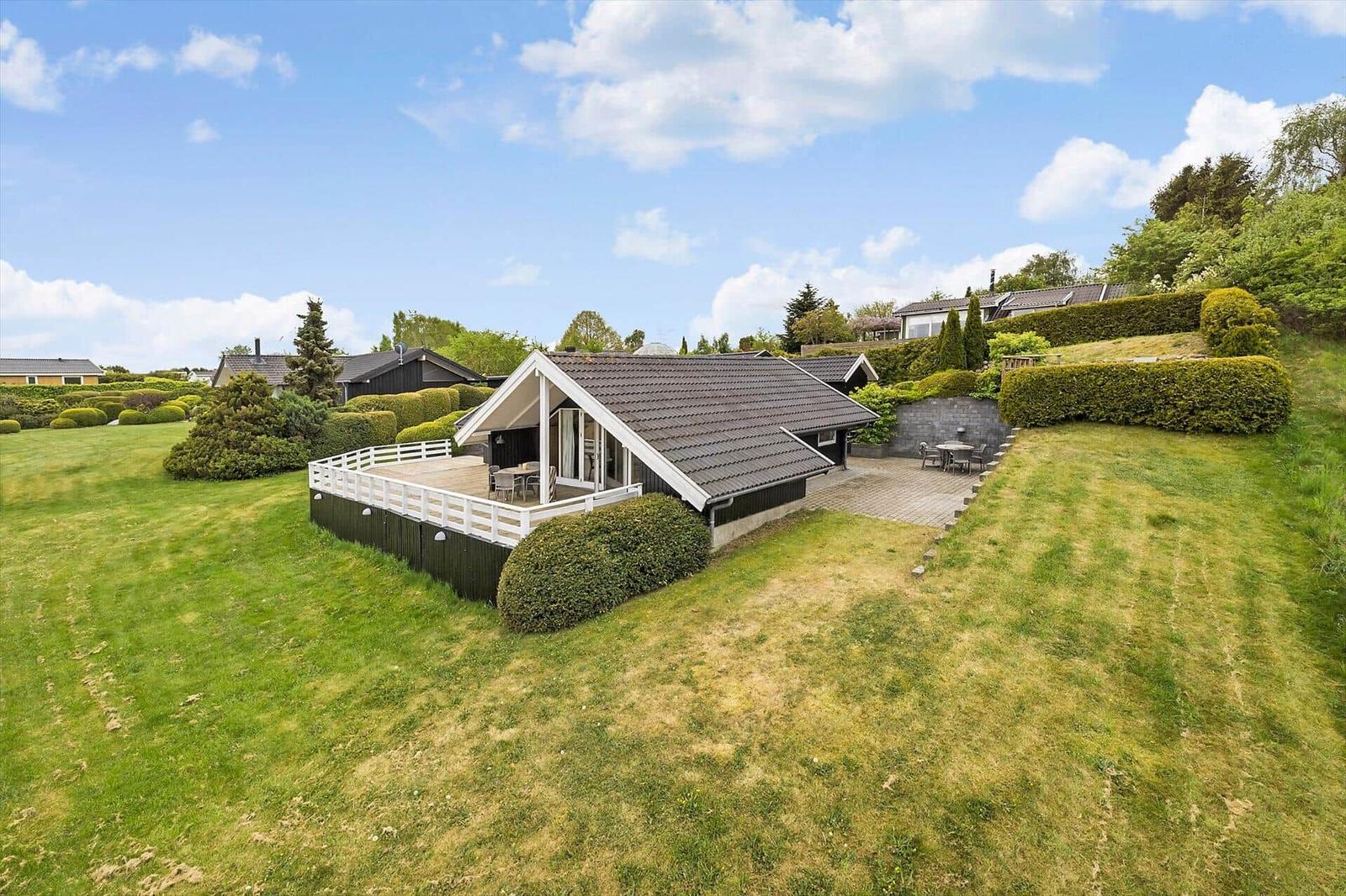 Haus mit Terrasse und Garten, umgeben von grüner Landschaft und Hecken.