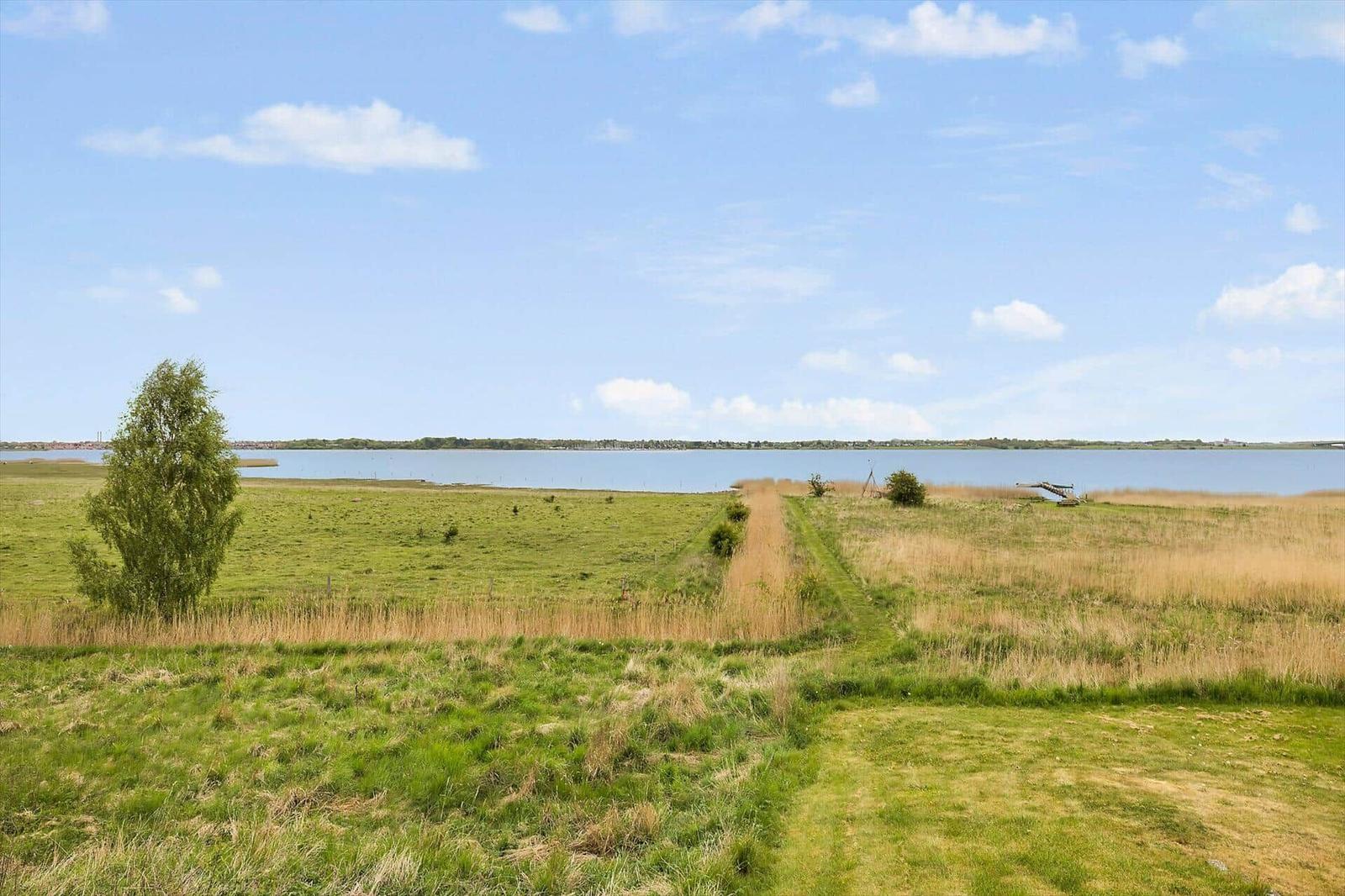 Weitläufiges Grasland mit Pfad zum Wasser unter blauem Himmel.