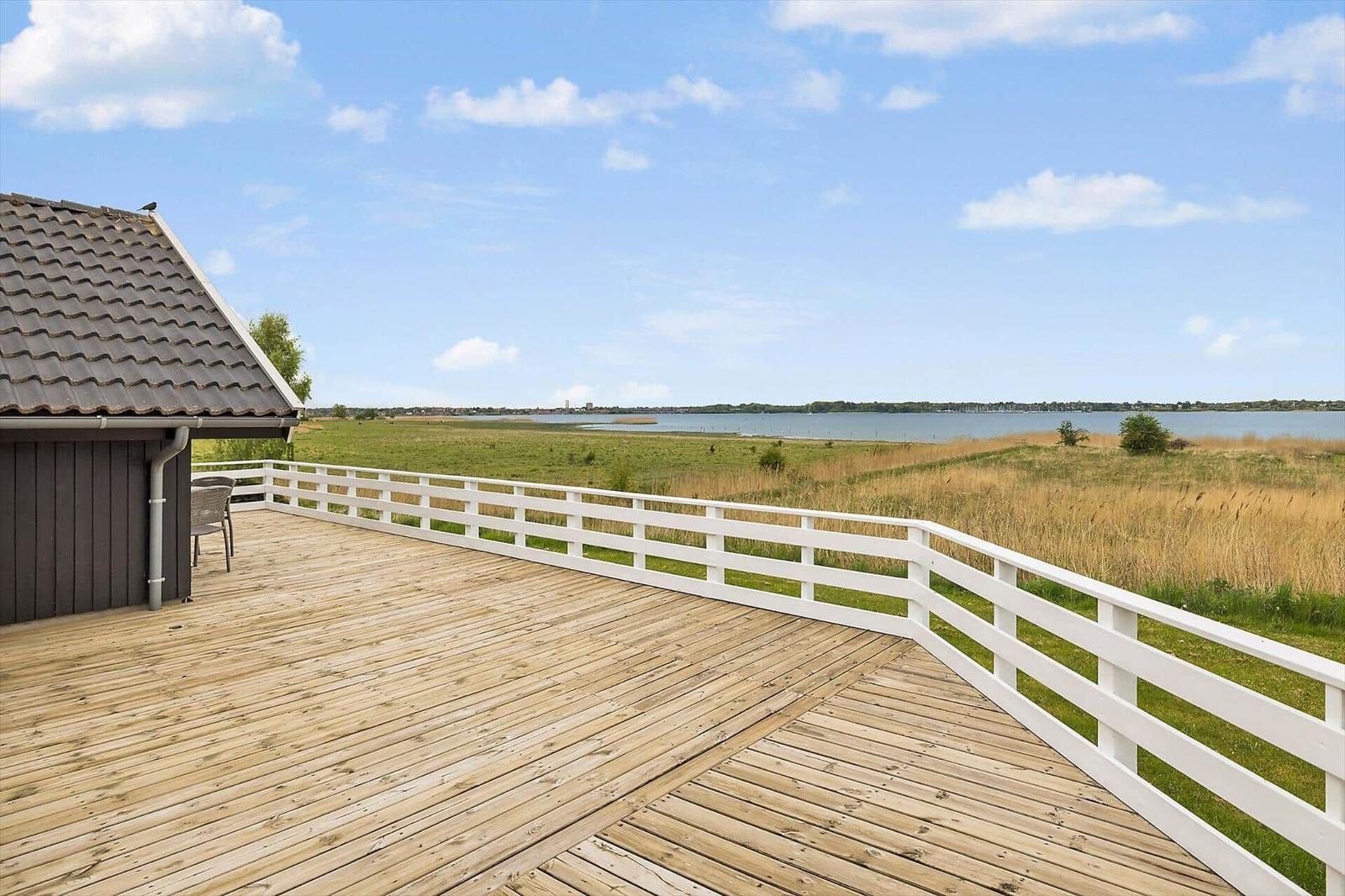 Holzterrasse mit weißem Geländer und Blick auf Wasser und Grasland.