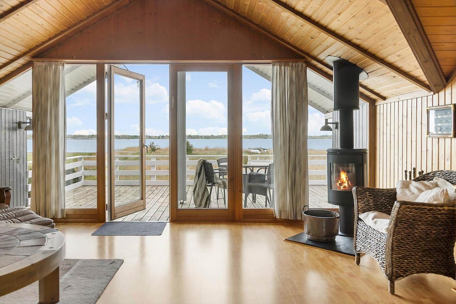 Wohnraum mit Kamin, Terrasse und Blick auf Wasser.