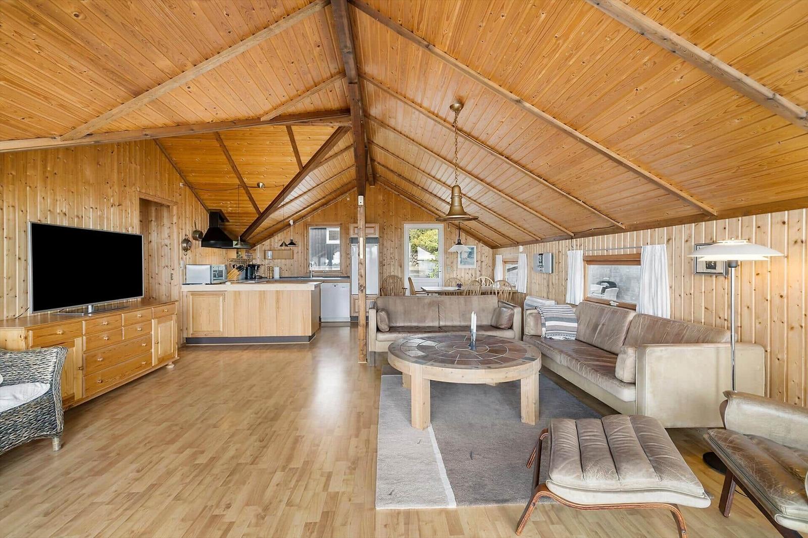 Wohnbereich mit Sofa, Esstisch und Küchenzeile unter Holzdecke.