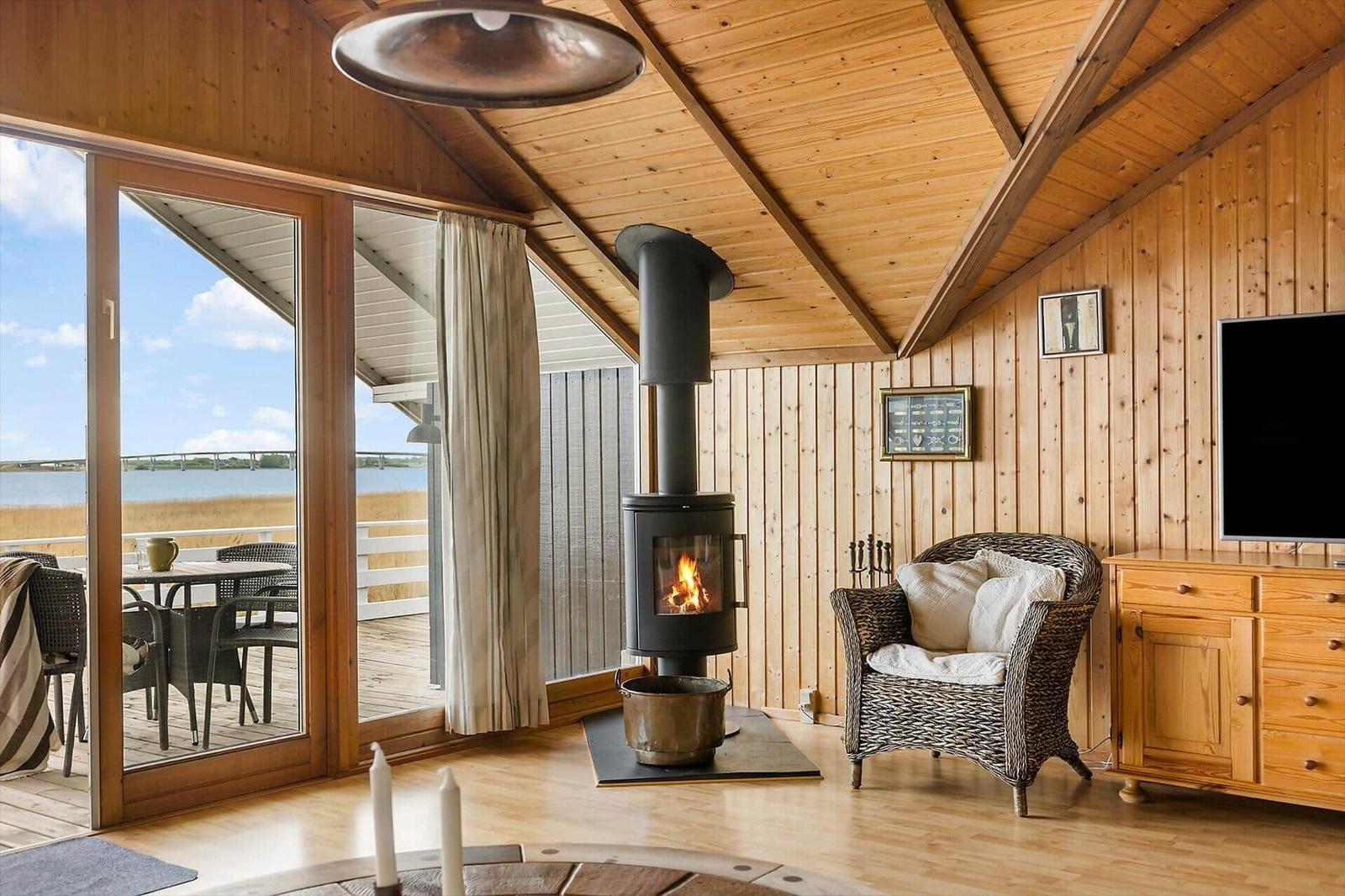 Wohnraum mit Kamin, Sessel und Terrasse mit Blick auf Wasser.