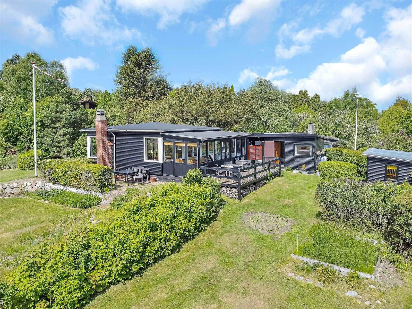 Schwarzes Haus mit Terrasse und Garten. Umgeben von Bäumen und Sträuchern.