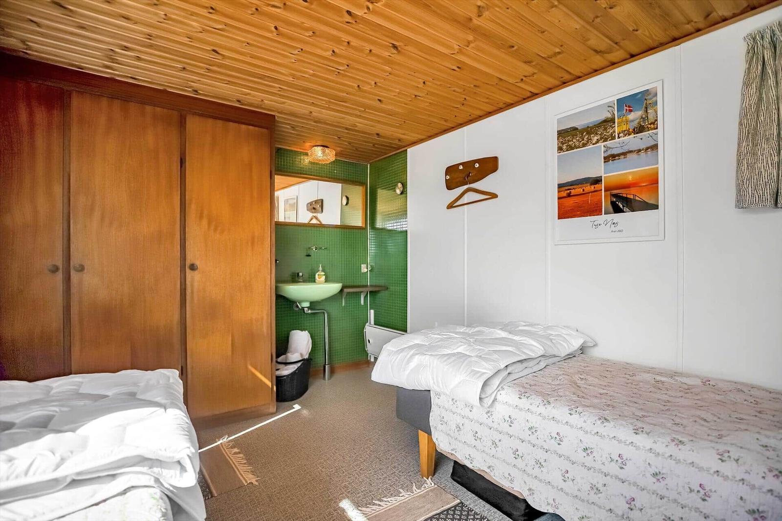 Zimmer mit zwei Betten, Holzdecke und integriertem Bad mit grüner Fliesenwand.