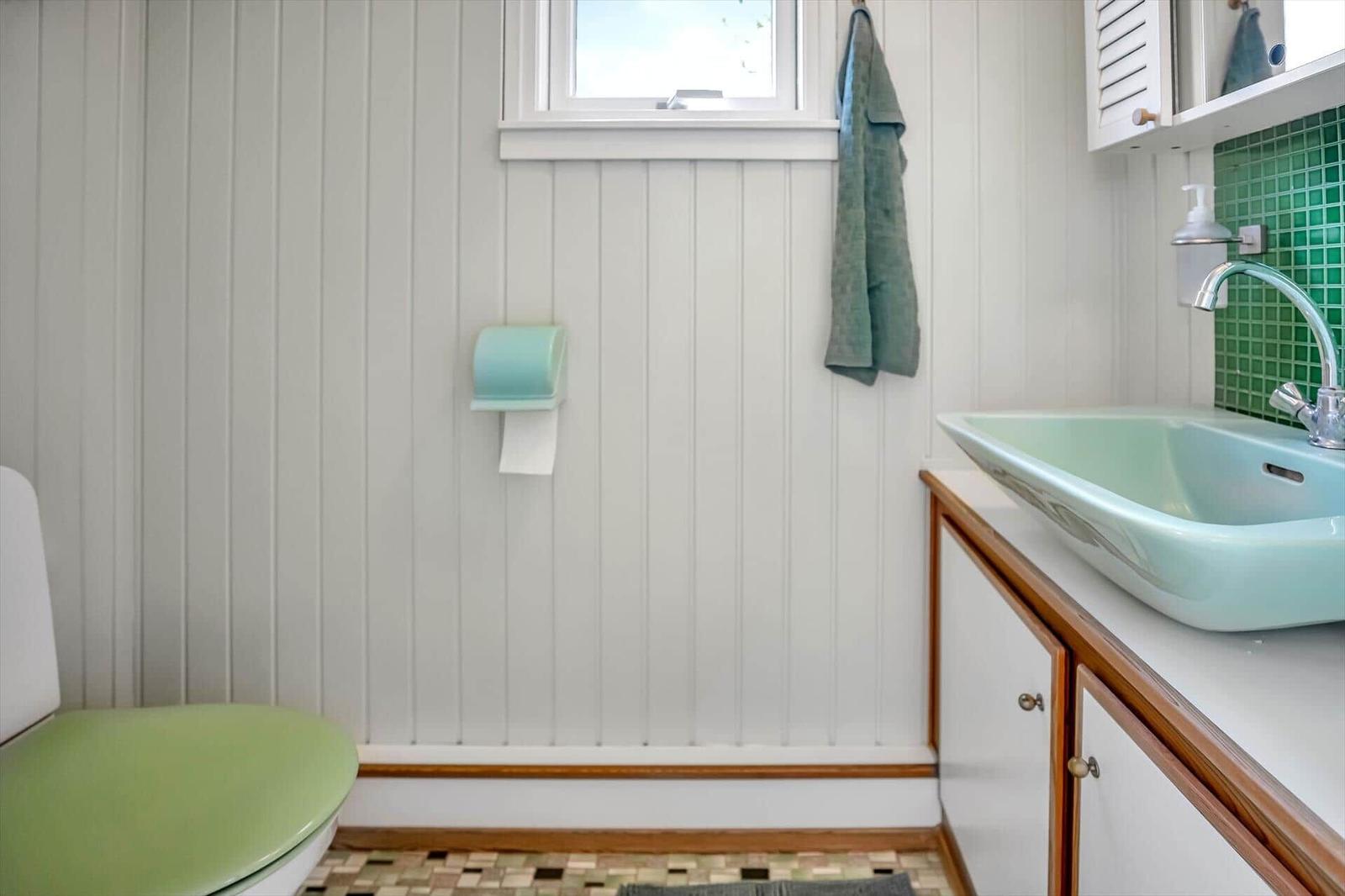 Badezimmer mit grünem Waschbecken, Toilette und grüner Handtuchhaken.
