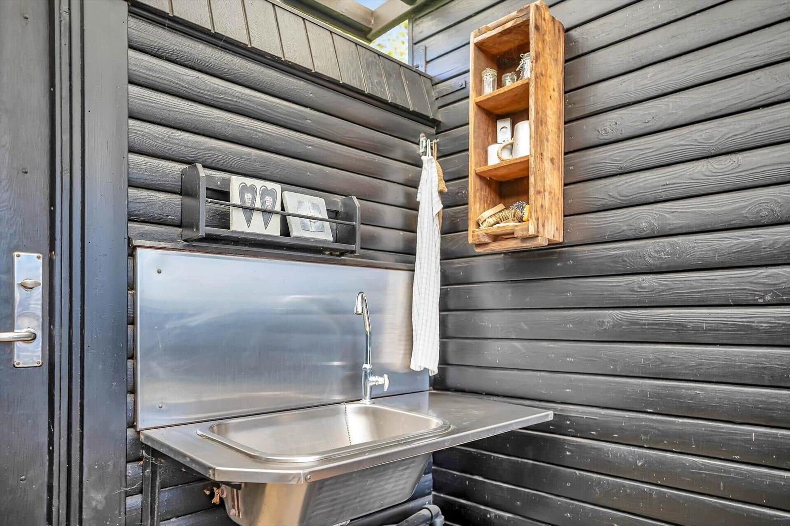 Außenwaschbecken mit Spüle und Haken für Handtücher an schwarzem Holzwandpaneel.