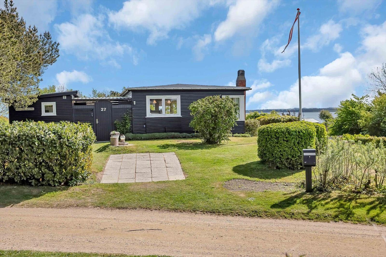 Schwarzes Haus mit Garten und Blick auf Wasser unter blauem Himmel.