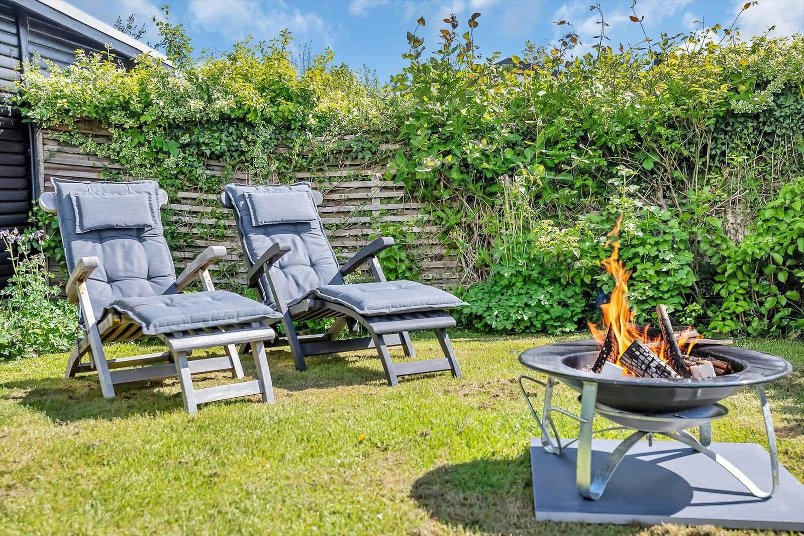Zwei Liegestühle und ein brennender Feuerkorb auf einer grünen Wiese.