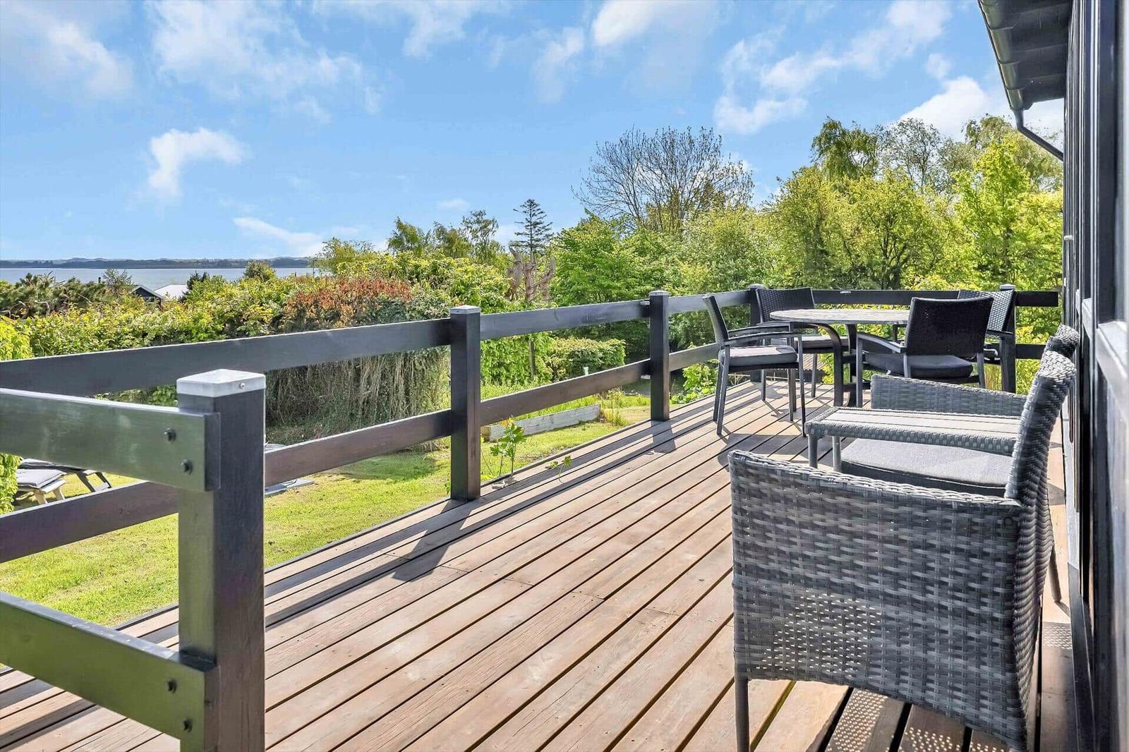 Terrasse mit Sitzgruppe und Blick auf Grünflächen und Wasser.
