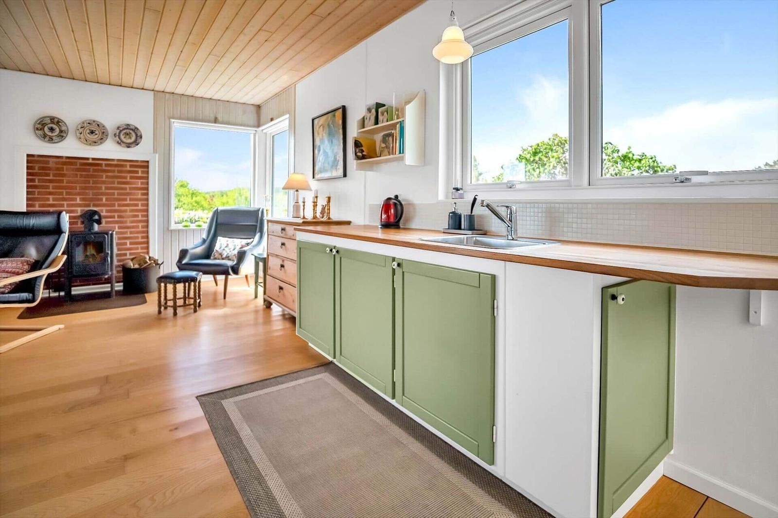 Küche mit grünen Schränken und Holzoberfläche. Blick auf Wohnzimmer mit Kamin und Sitzgelegenheiten.