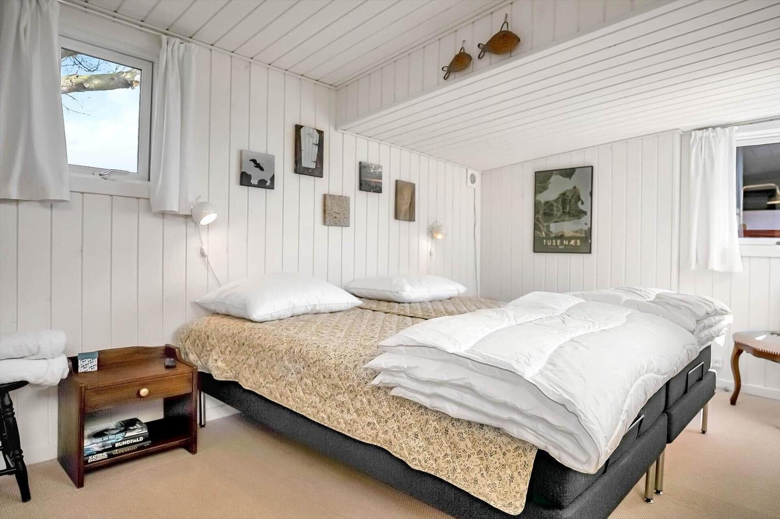 Schlafzimmer mit Doppelbett, weißen Wänden und Fenstern mit Vorhängen.