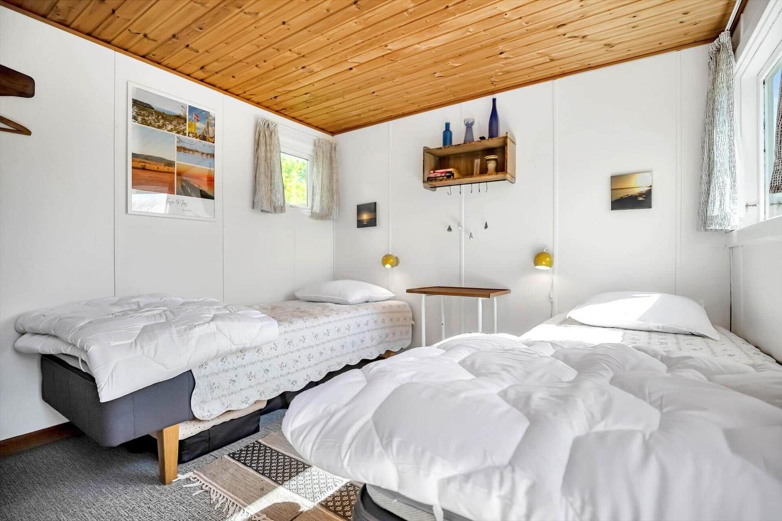 Zwei Betten mit weißen Bettdecken und gemusterten Laken. Holzdecke und Wandregal mit Dekorationsgegenständen.