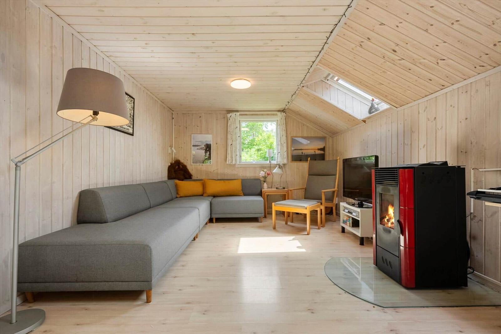Wohnzimmer mit Sofa, Kamin und Fenster. Holzwände und -decke.